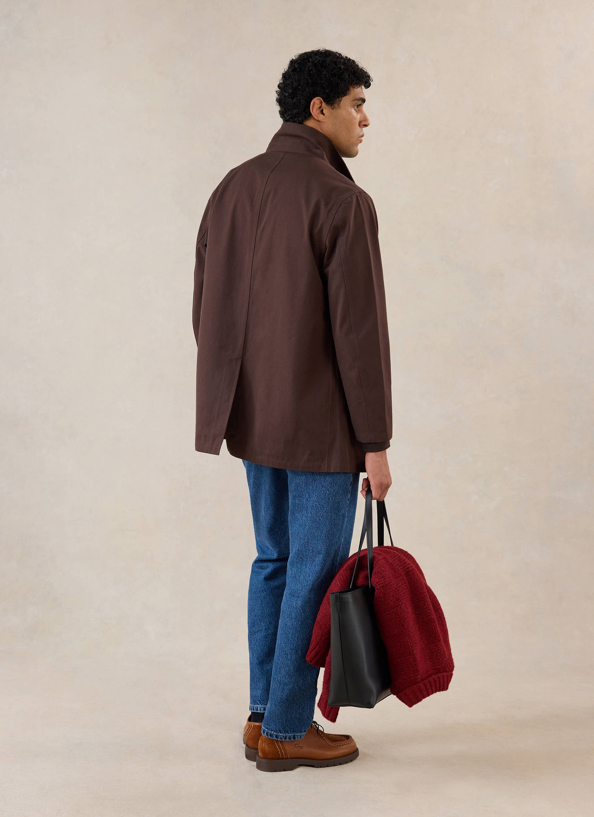 A model from the back wearing the Percival espresso brown Sherlock short trench coat, blue jeans, and holding a tote bag.