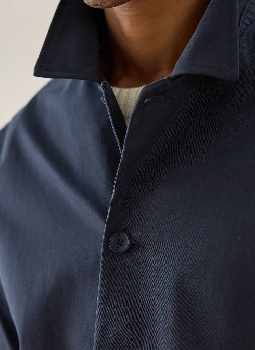Close-up of the navy Percival Sherlock short trench coat collar and button fastening on a model.