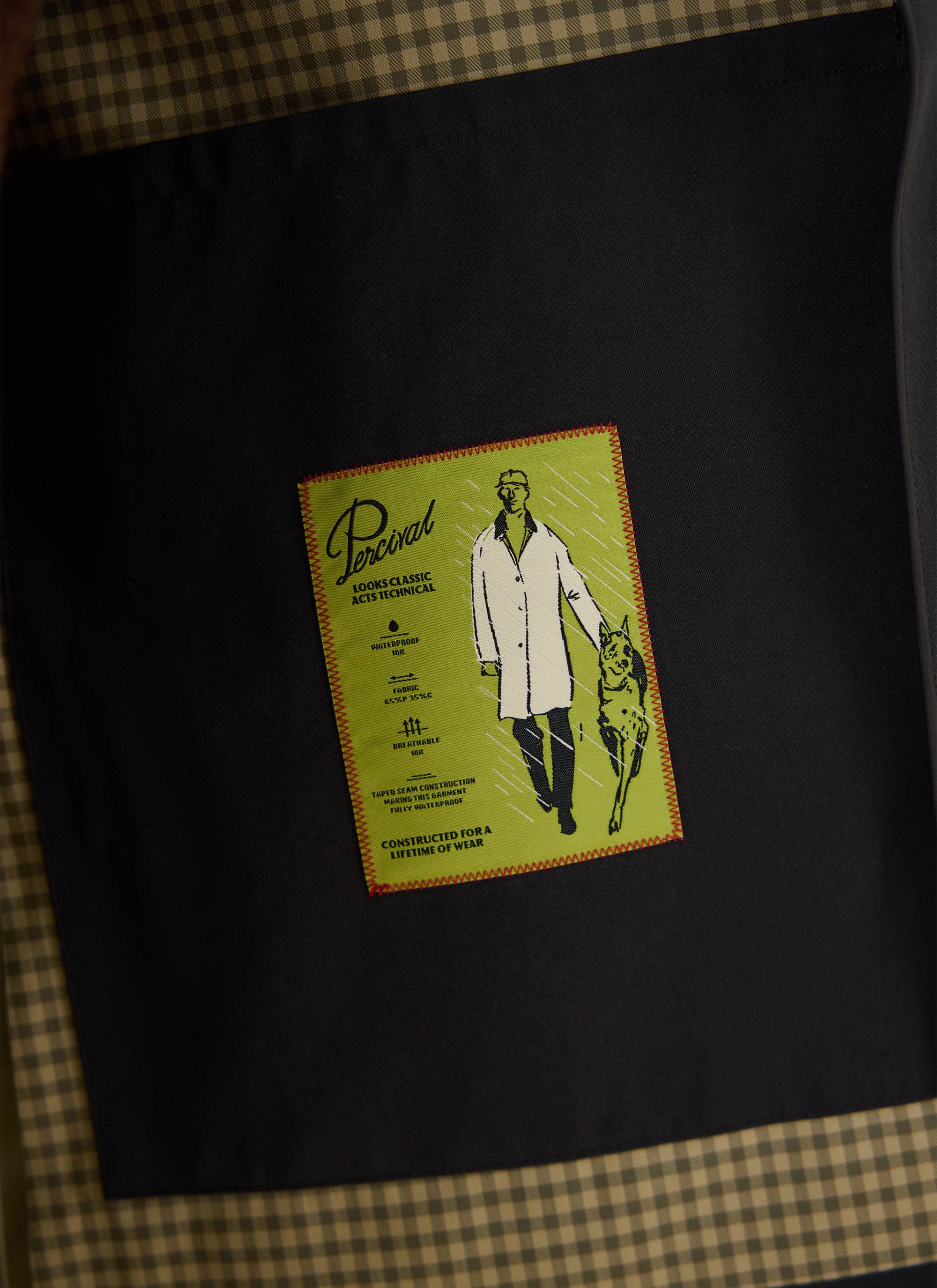 A close-up of the screen printed technical details label inside the black Percival Sherlock Short Trench Coat.