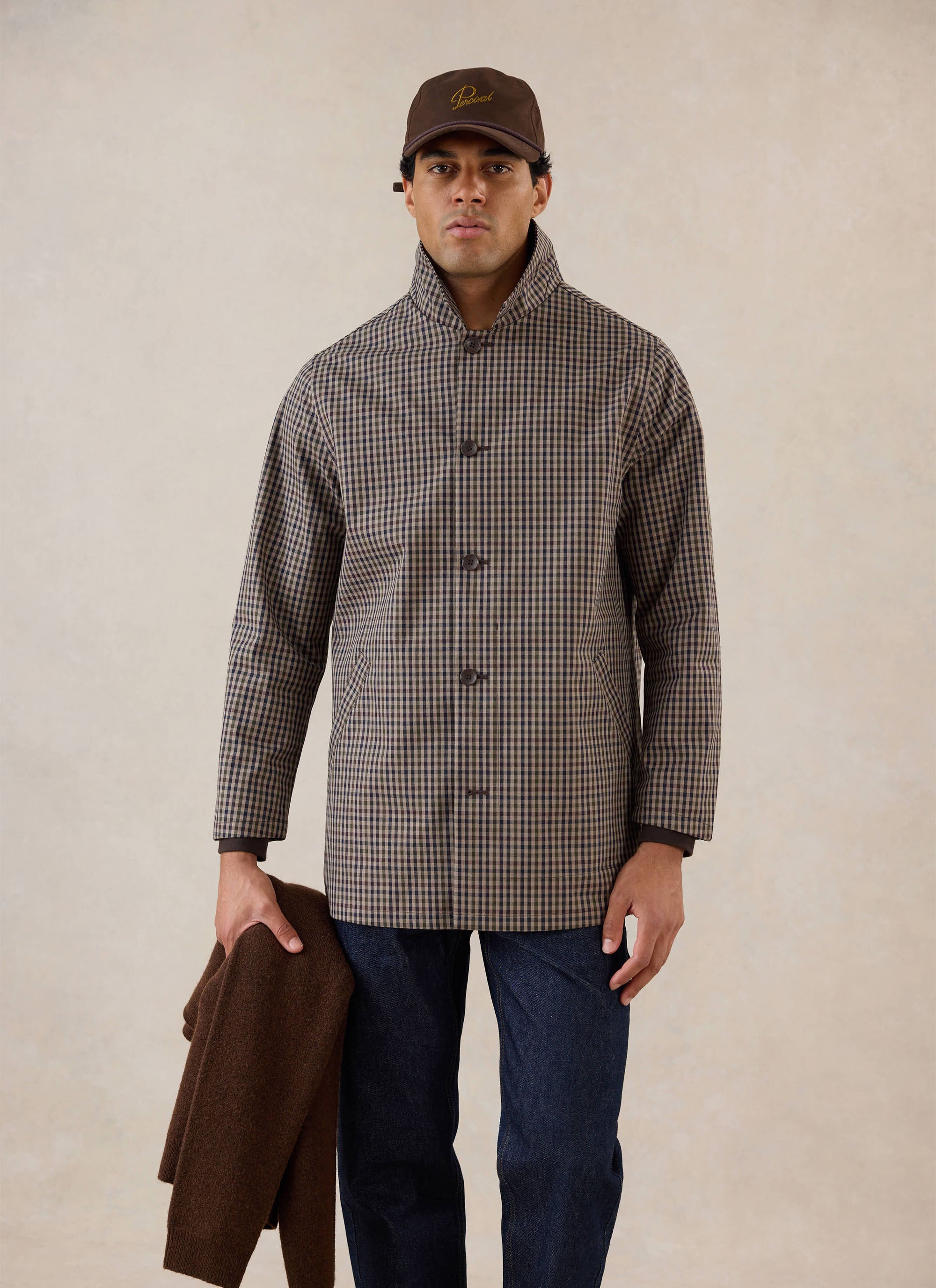 A model wears the Percival Watcher Check Sherlock Short Trench Coat with a brown cap and denim jeans in a studio shot.