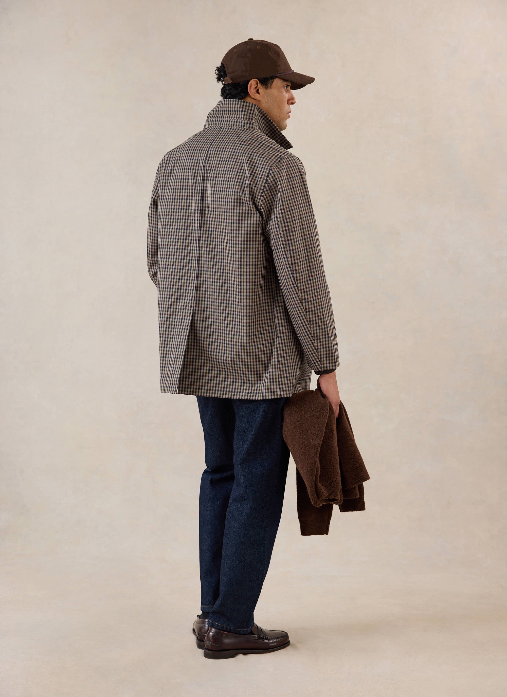 A model from behind wearing the Percival Sherlock Short Trench Coat in Watcher Check, paired with dark trousers and a cap.