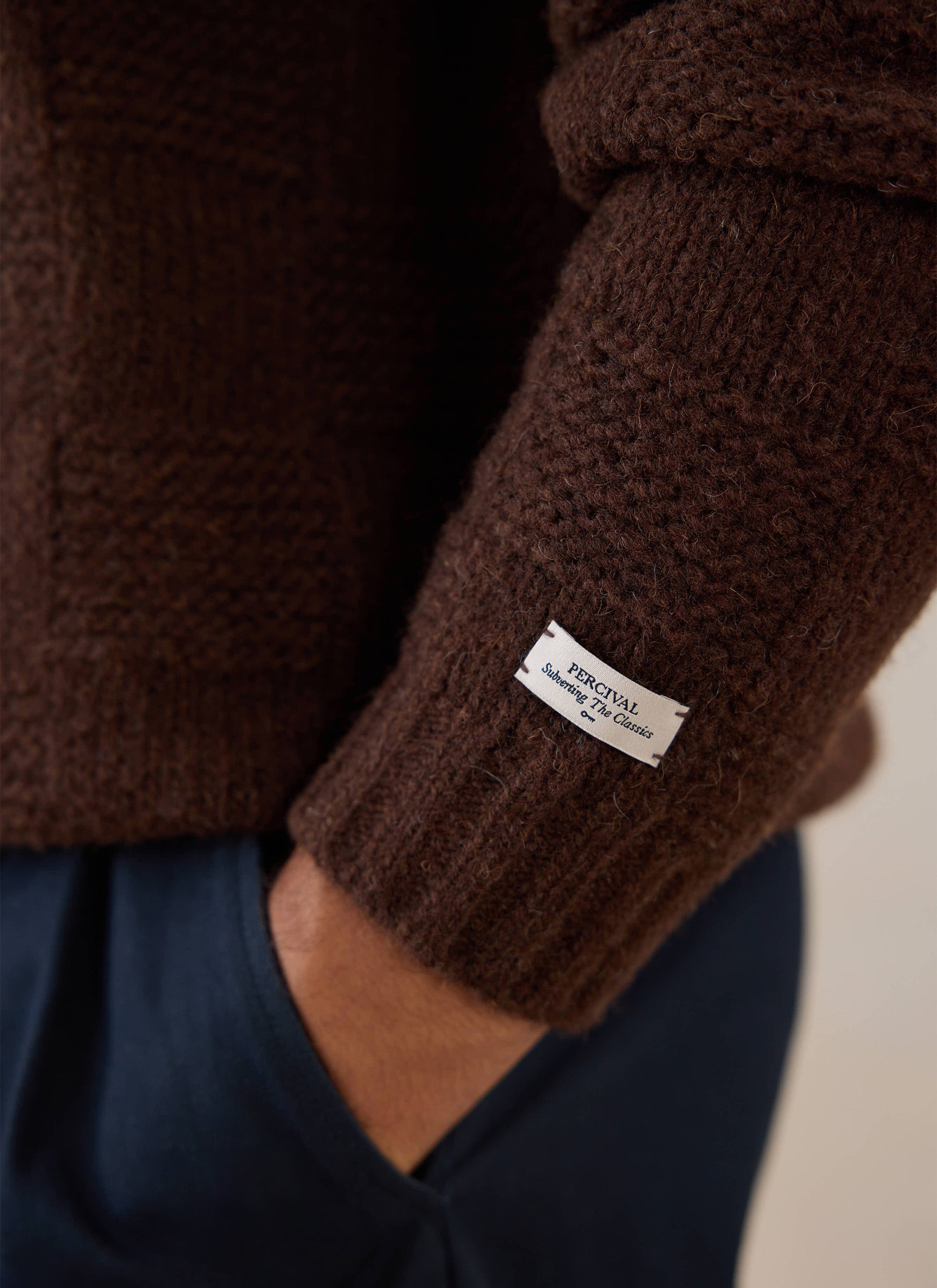 A close-up of the brown Percival Shugart Knit Jumper, highlighting the textured alpaca blend and branded label on the sleeve.