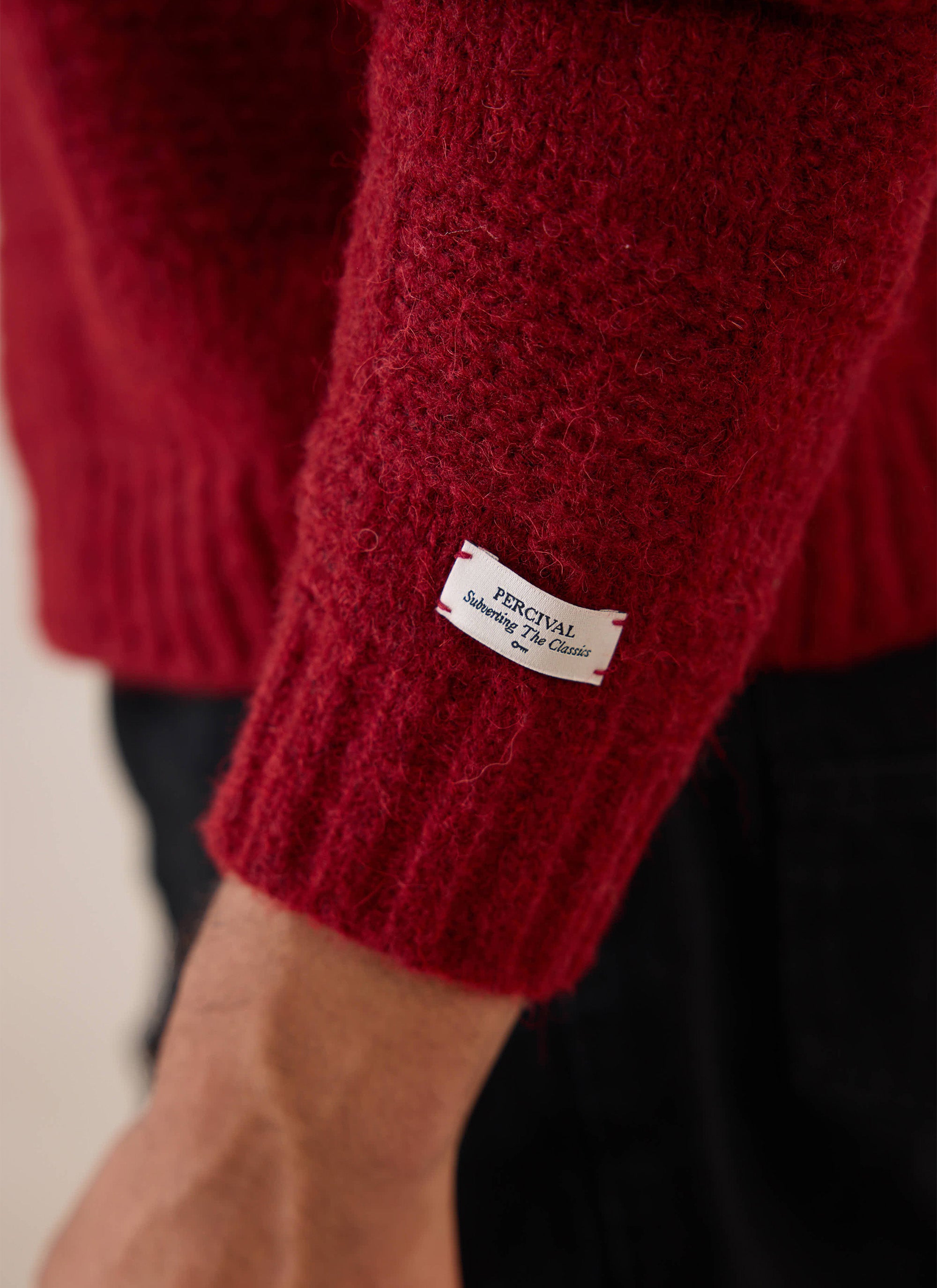 A close-up of the sleeve label on the burgundy Percival Shugart Knit Jumper.