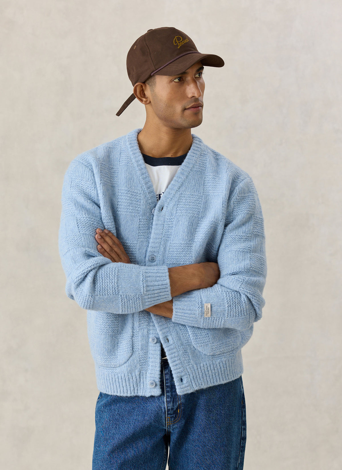 A model wearing the Percival light blue alpaca wool blend Shugart cardigan with a brown cap and blue jeans.