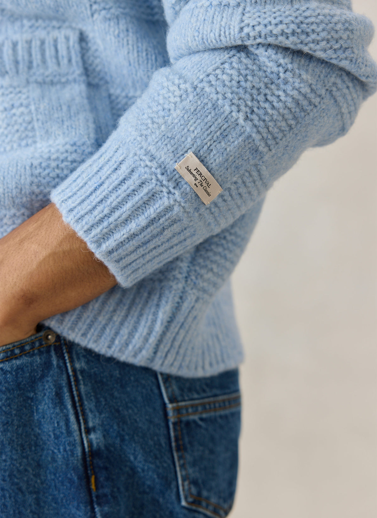 A close-up of the Percival light blue alpaca wool blend Shugart cardigan sleeve, showing the ribbed cuff and branded label.