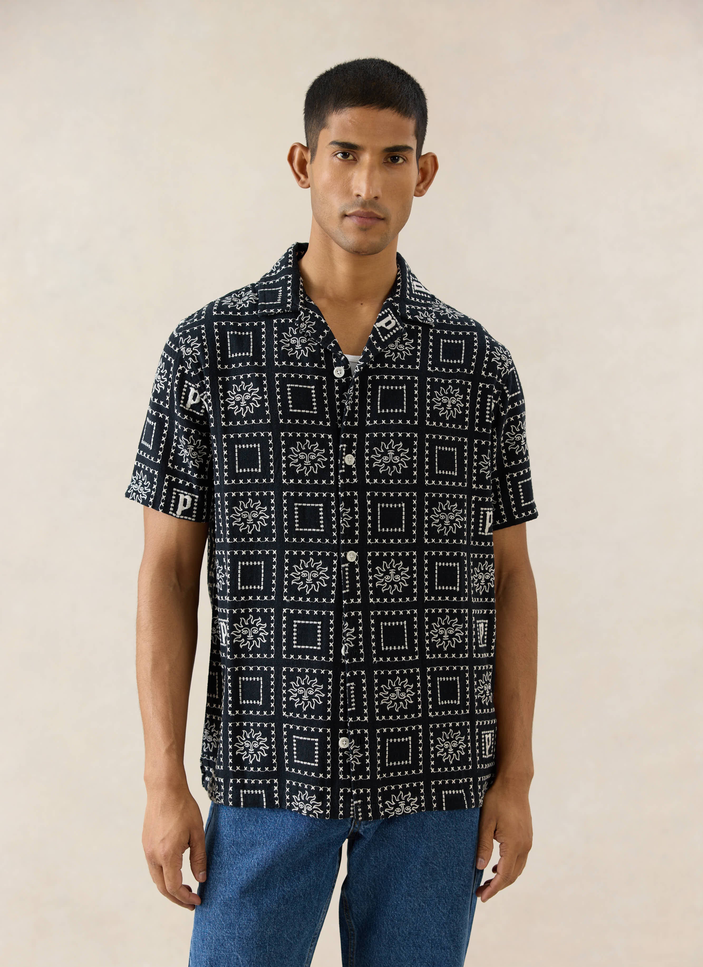 Percival Solis Heaton Cuban Shirt in black linen blend, featuring white embroidered sun motifs, shown on a model.