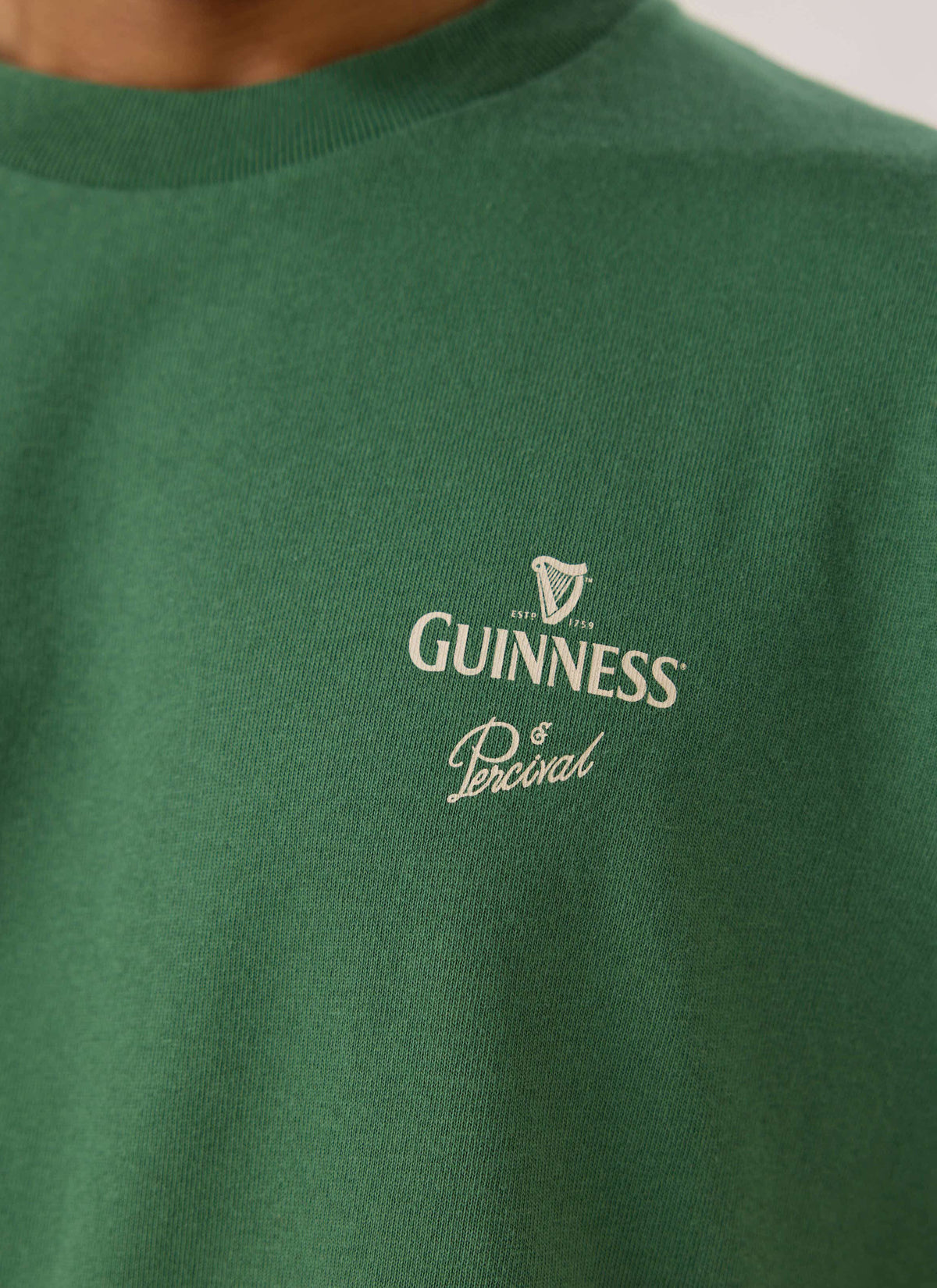 A close-up of the forest green Guinness x Percival T-shirt showing the white chest print detail.