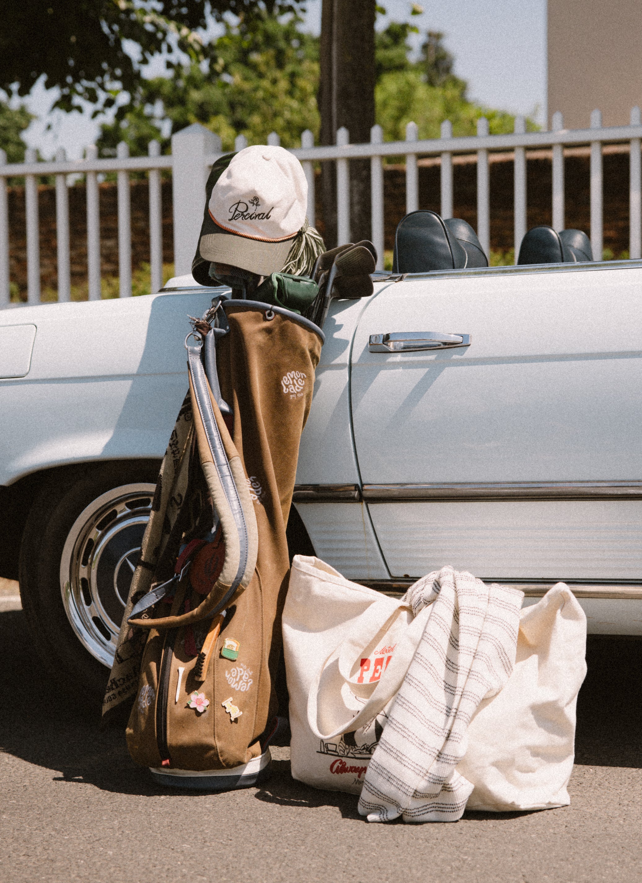 The cream Percival Spencer brushed cotton cap sits on a golf bag next to a Gordon tote and vintage car.