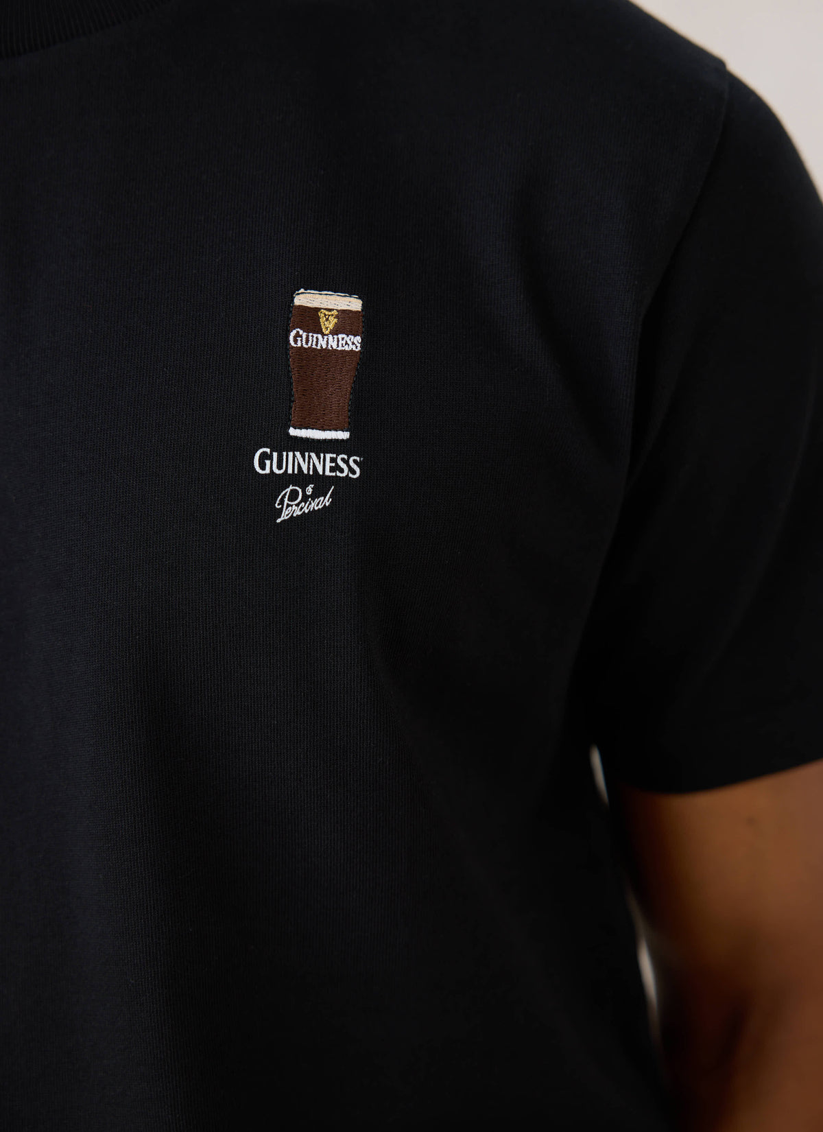 A close-up of the black Guinness x Percival Stout T-Shirt showing the hand-illustrated pint embroidery and logo on the chest.
