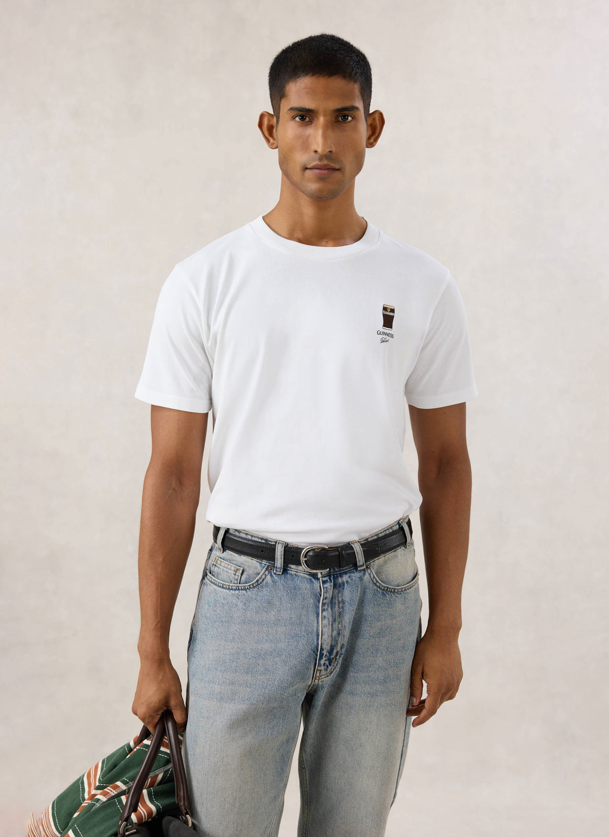 Model wearing the white Guinness x Percival stout embroidered organic cotton t-shirt with blue jeans.
