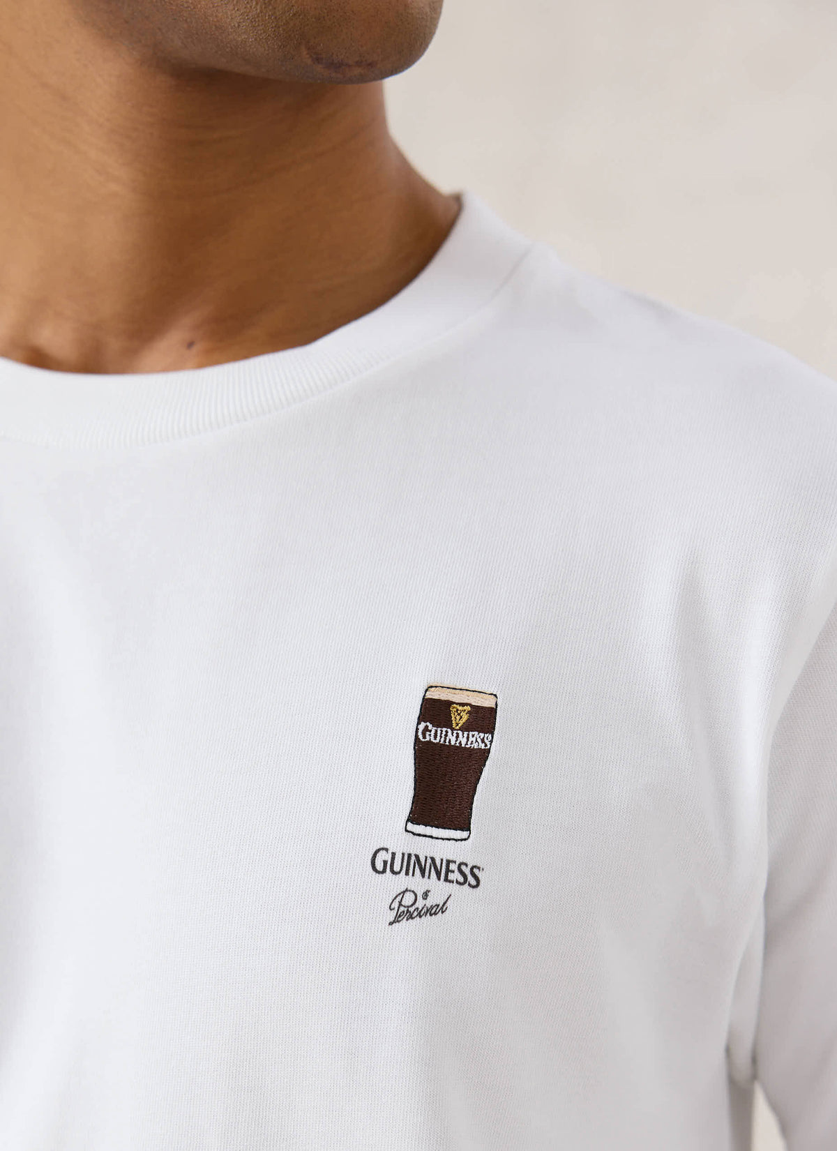 A close-up of the white Guinness x Percival stout embroidered T-shirt showing the chest graphic detail.
