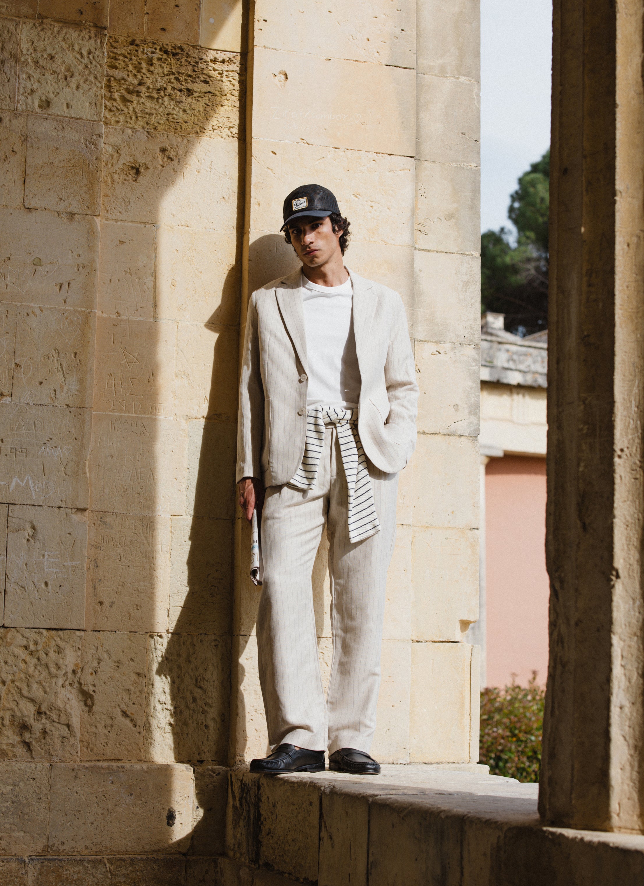 A model wears the cream striped linen blend suit from Percival, featuring a tailored blazer and trousers.