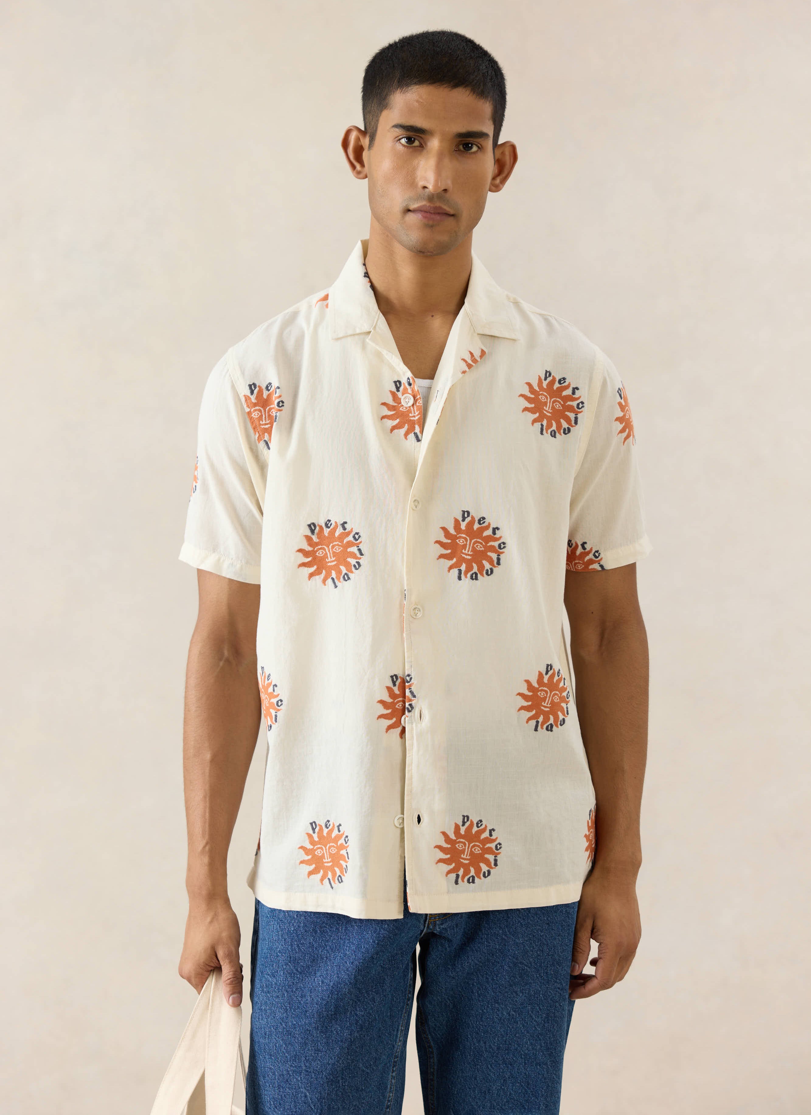 The Percival Sun Cuban Shirt in cream cotton with orange sun embroidery, styled on a model with blue jeans.