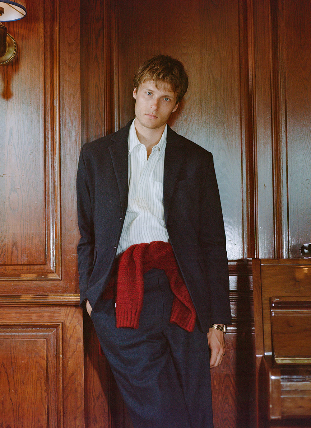 A model wears the navy herringbone wool Percival blazer and trousers, styled with a red sweater tied around the waist.