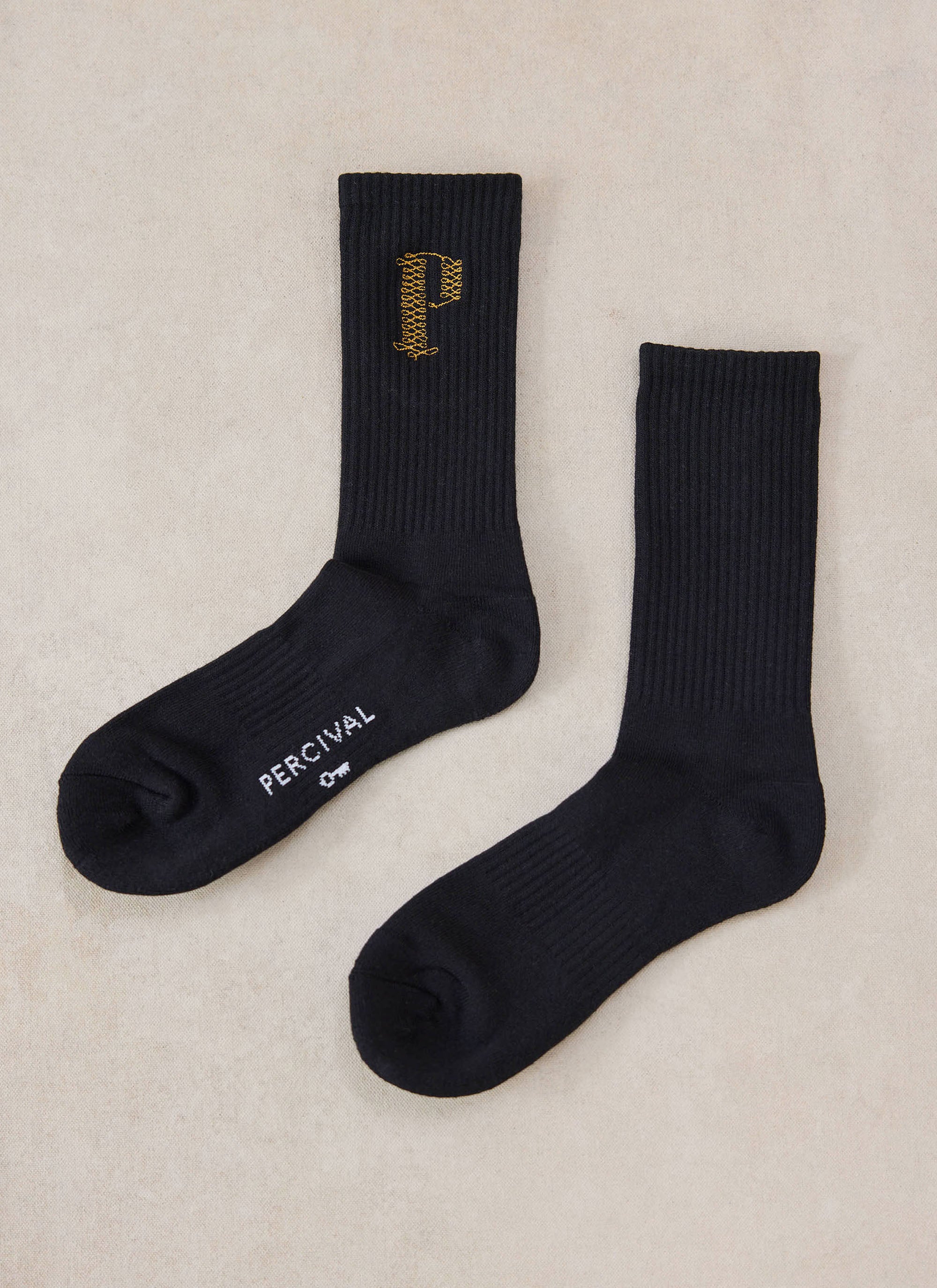 A pair of black Tucker embroidered socks with gold detailing from Percival laid flat on a neutral background.