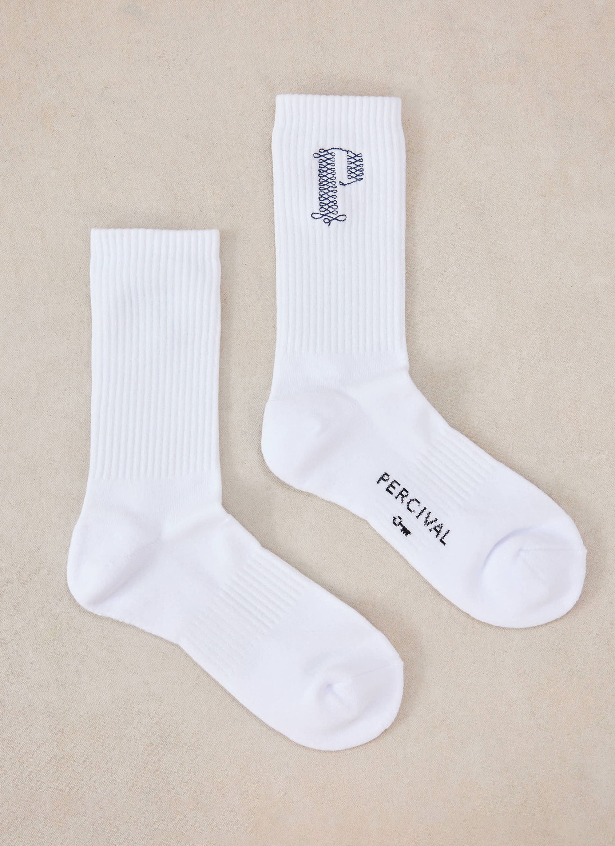 A flat lay of the white Tucker embroidered socks from Percival with blue detailing on a neutral background.