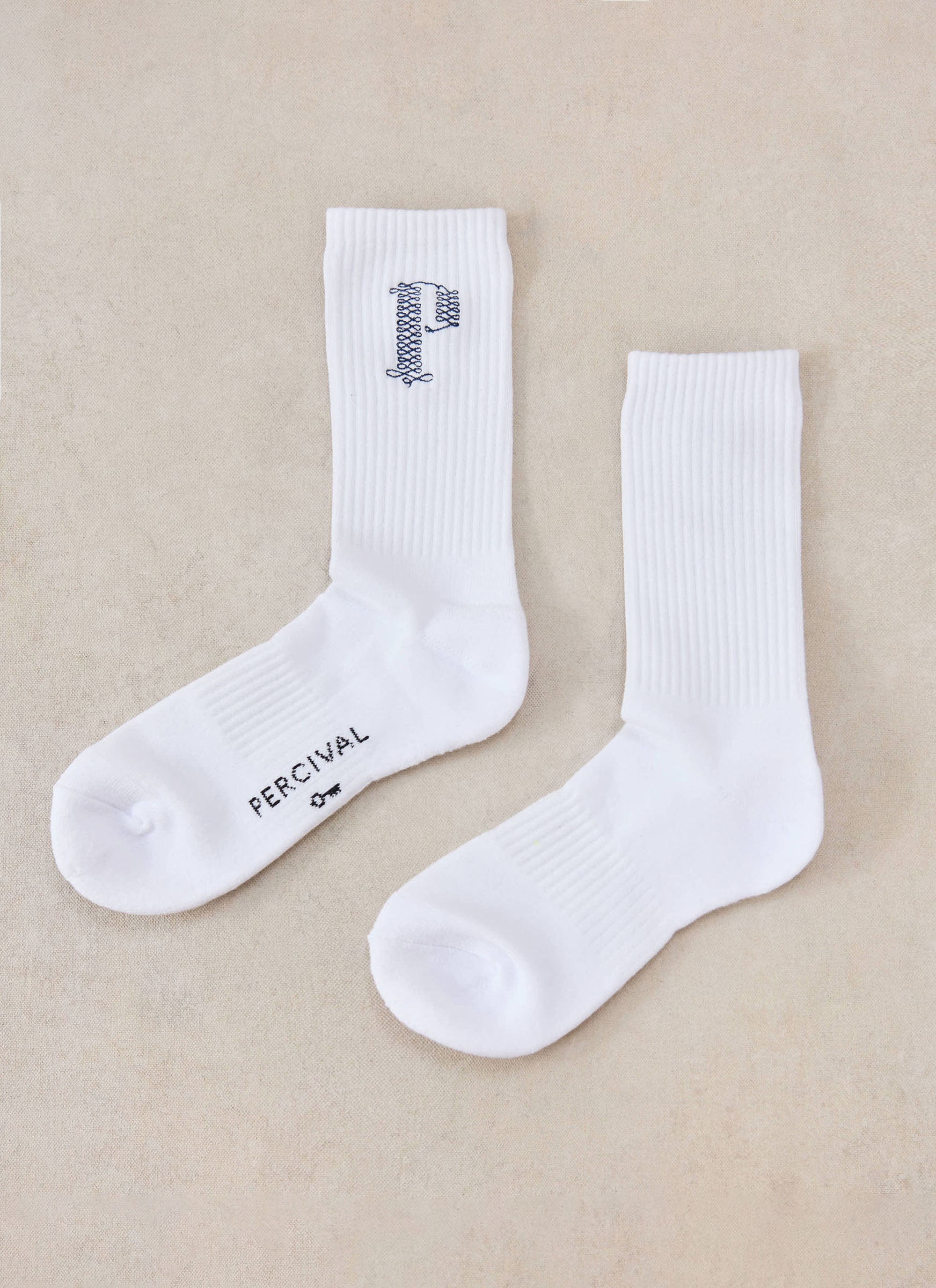A flat lay of the white Percival Tucker embroidered socks, showing the side profile, ribbed texture and branding.