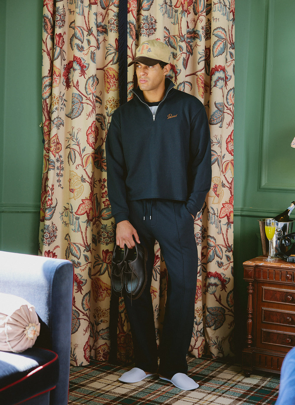 A model wearing the navy Percival Conrad 1/4 zip jumper and matching trackpants, styled with a Tucker cap.