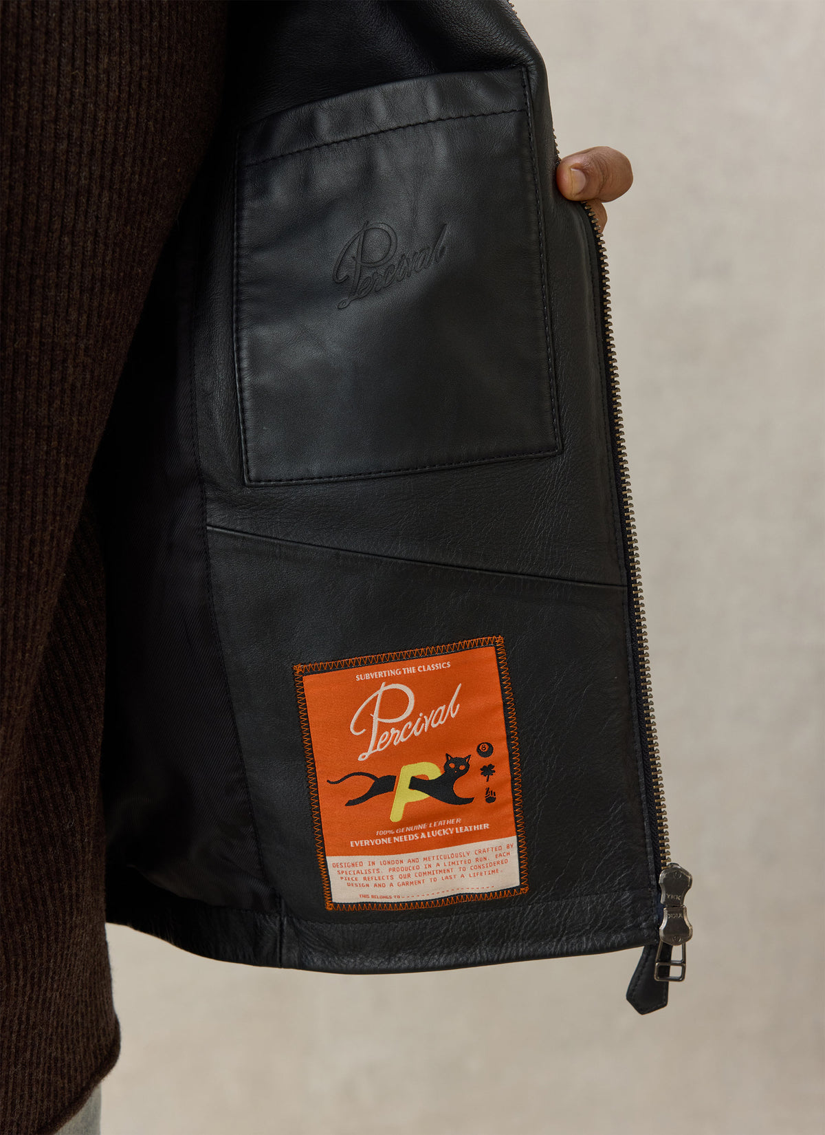 A close-up of the interior of the Percival black leather jacket showing the custom internal patch label and pocket.