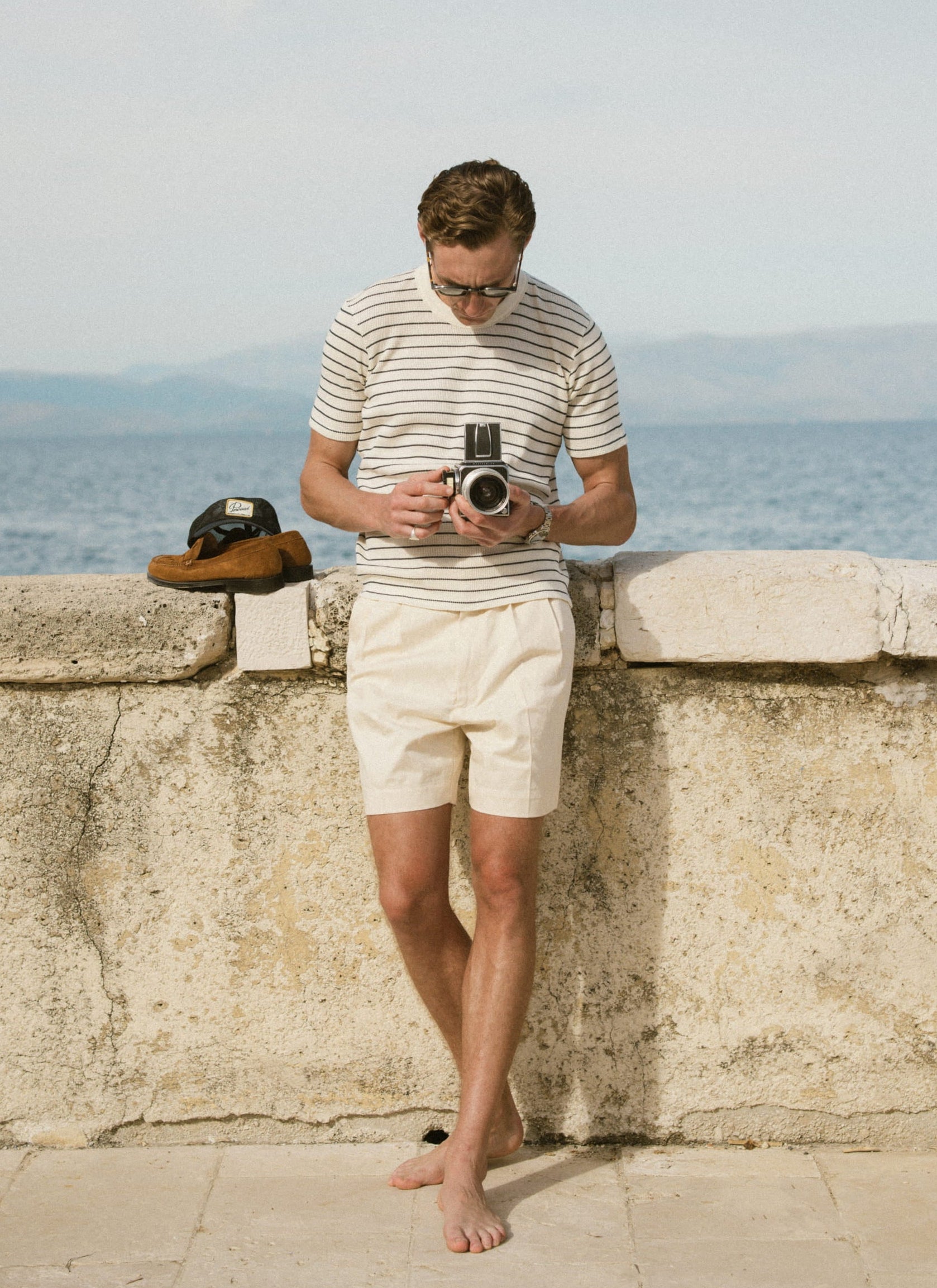 Model wearing the textured Percival Ernie Waffle T-shirt in cream stripe and Blake shorts in a coastal setting.