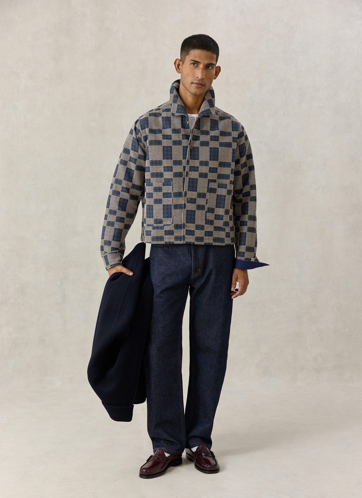 A model wearing the navy and cream Wallis grid check overshirt in cotton with dark jeans against a neutral studio backdrop.