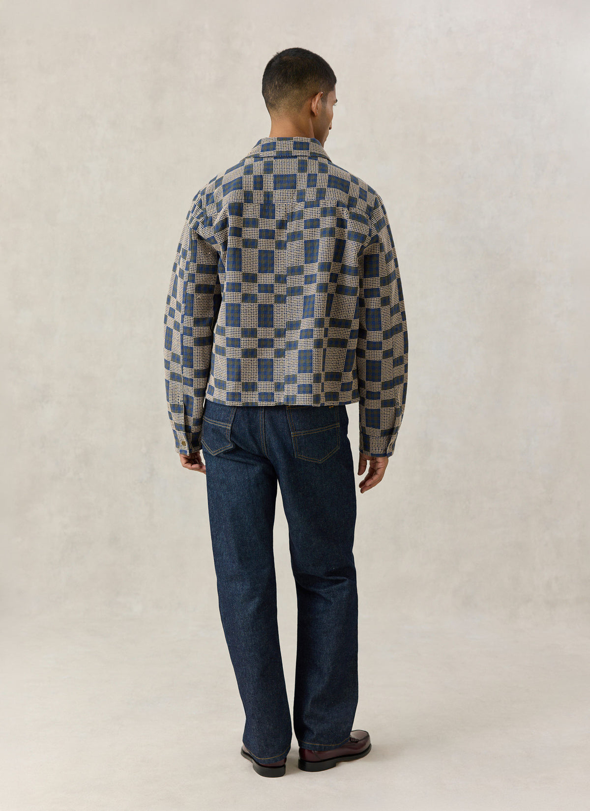 A model from the back wearing the Percival Wallis grid check overshirt in navy blue and cream, paired with dark jeans.