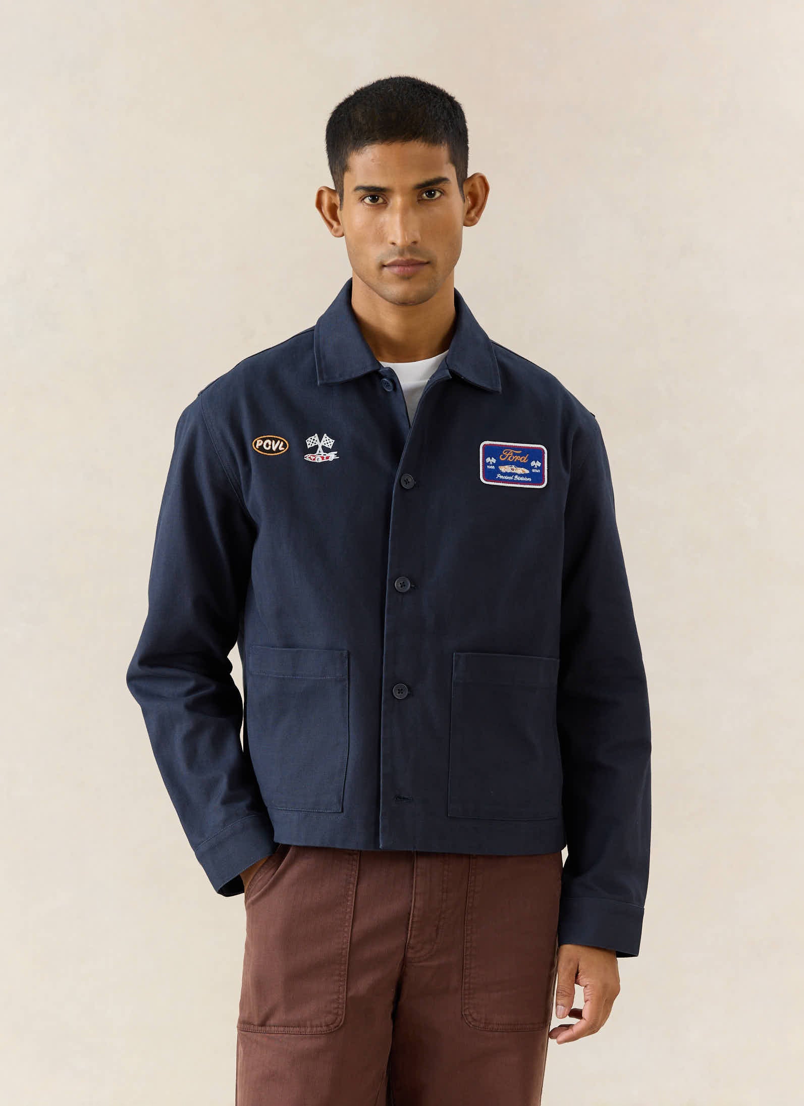 Navy Ford x Percival embroidered canvas jacket featuring GT40 motorsport patches, styled with brown trousers.