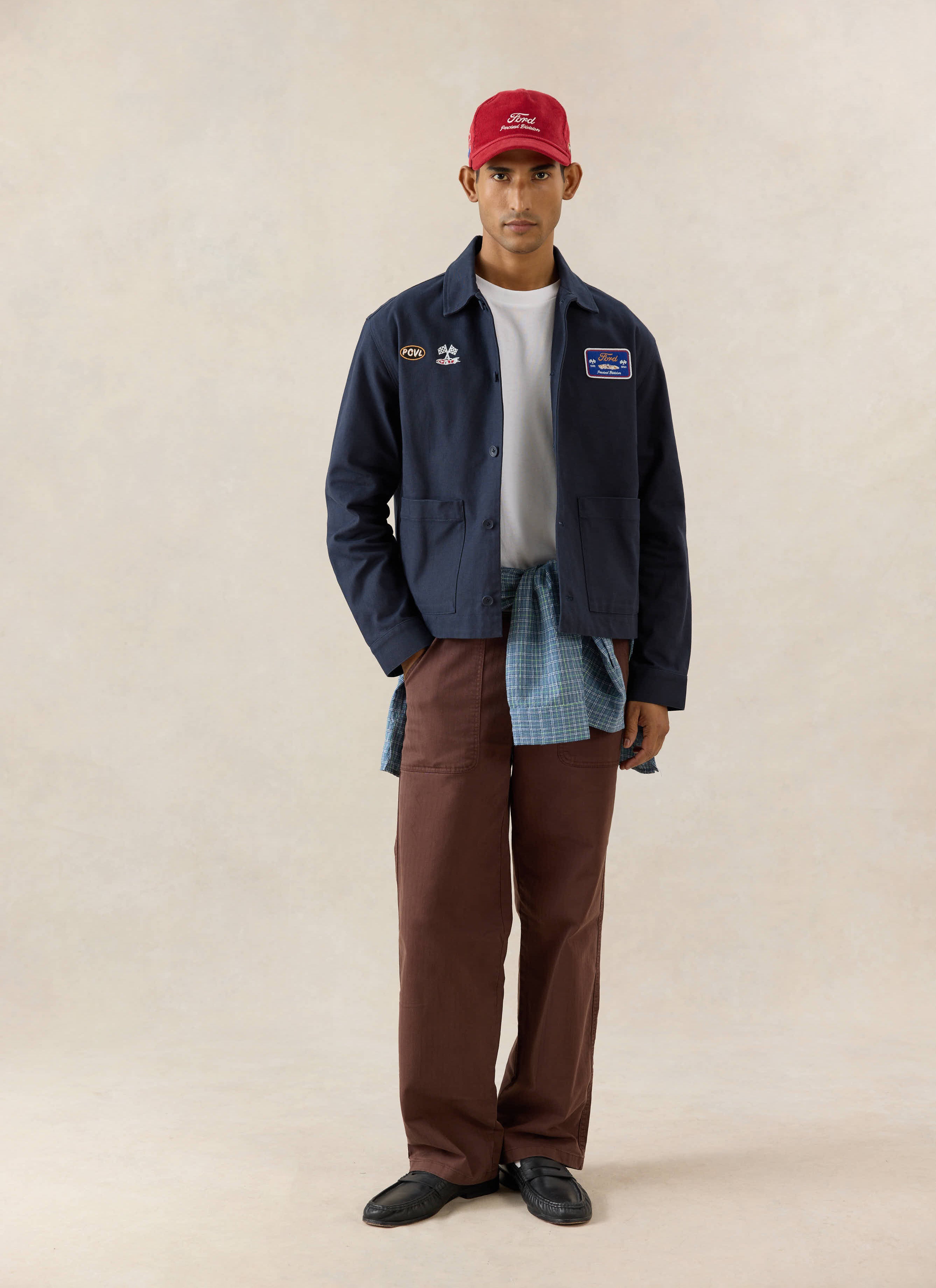 Navy Ford x Percival GT40 Embroidered Canvas Jacket styled with brown trousers and a red cap in a studio shot.