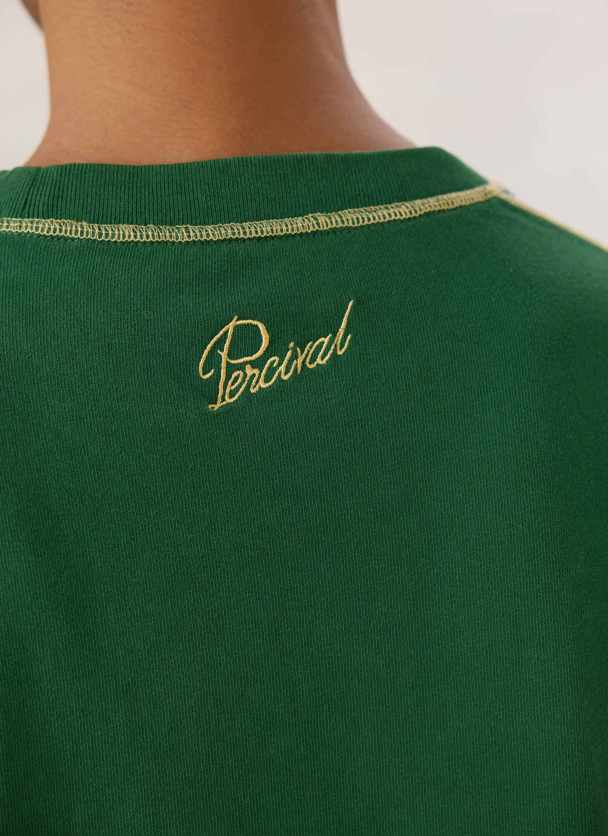 Close-up of back neck showing Percival script embroidery and stitching on the forest green t-shirt.