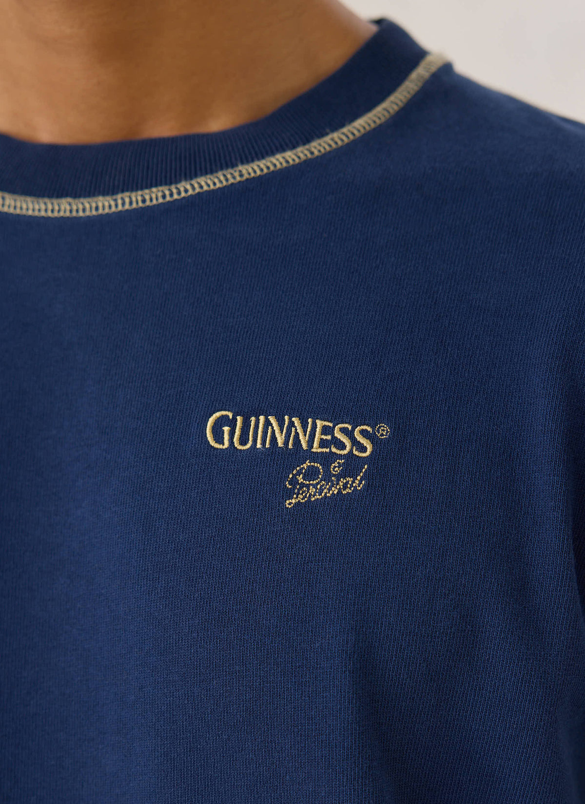 Close-up of the navy Guinness x Percival cotton T-shirt, highlighting the gold chest embroidery and contrast stitching.