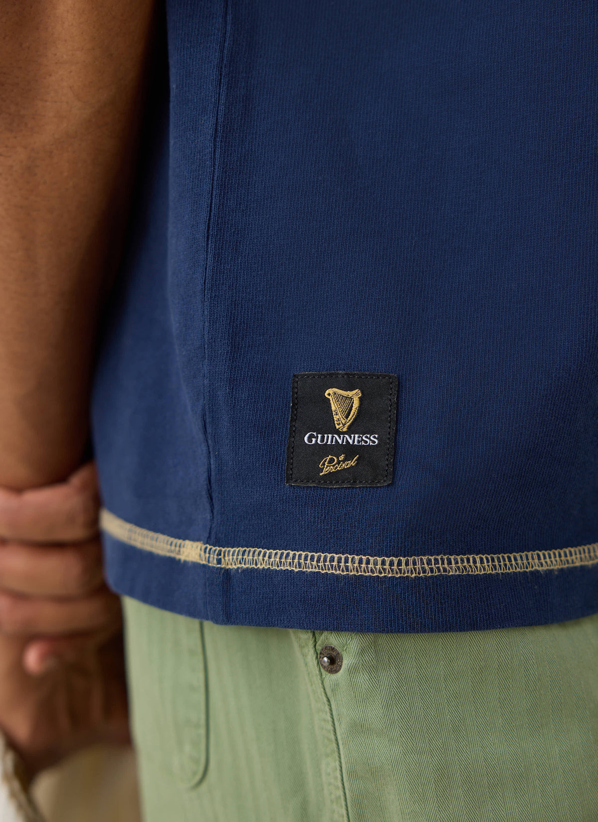 Close-up of the navy Guinness x Percival vintage wash T-shirt showing the woven hem label and contrast flatlock stitching.