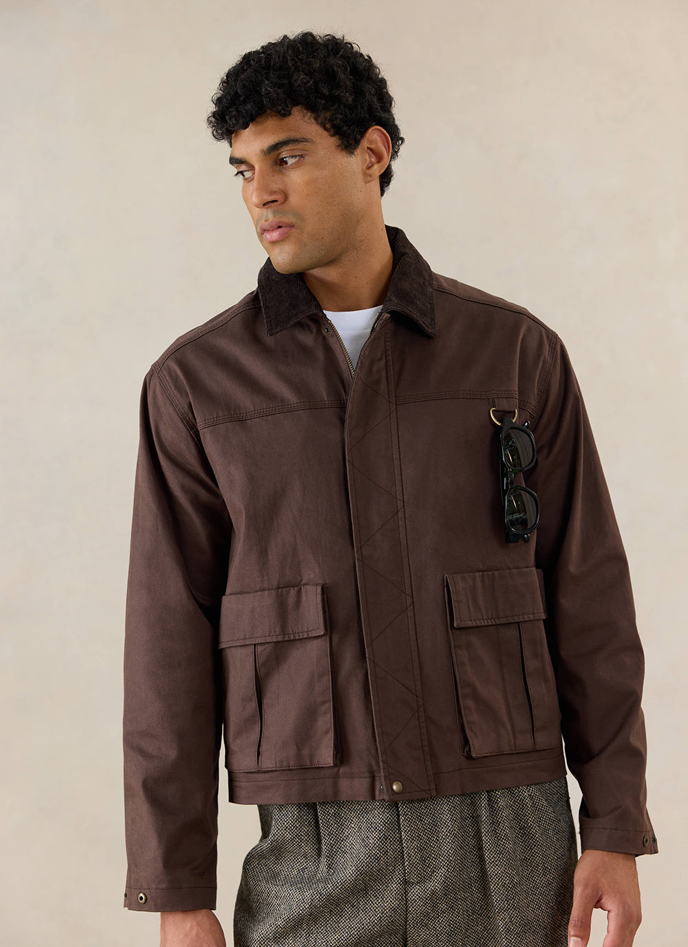 A model wears the Percival wax zip jacket in espresso brown cotton with utility patch pockets and a dark corduroy collar.