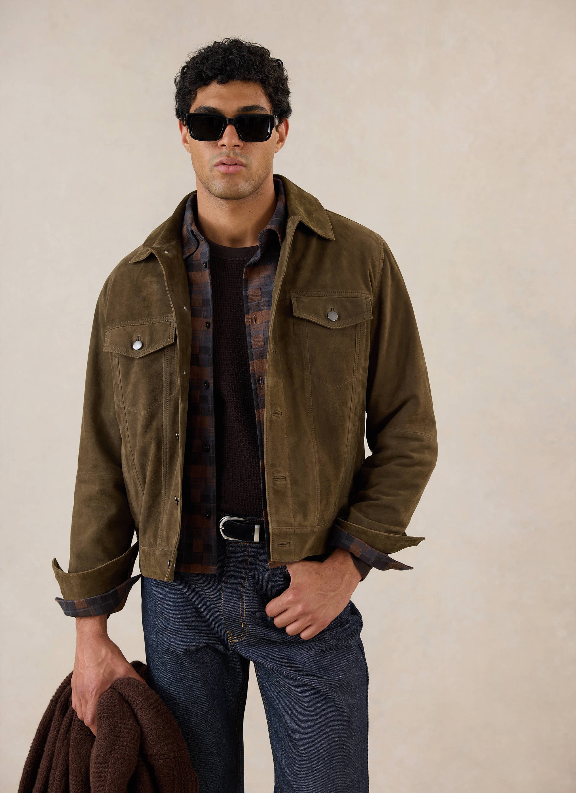 A model wears the olive Percival suede western jacket, styled with a patterned shirt, dark jeans and sunglasses.