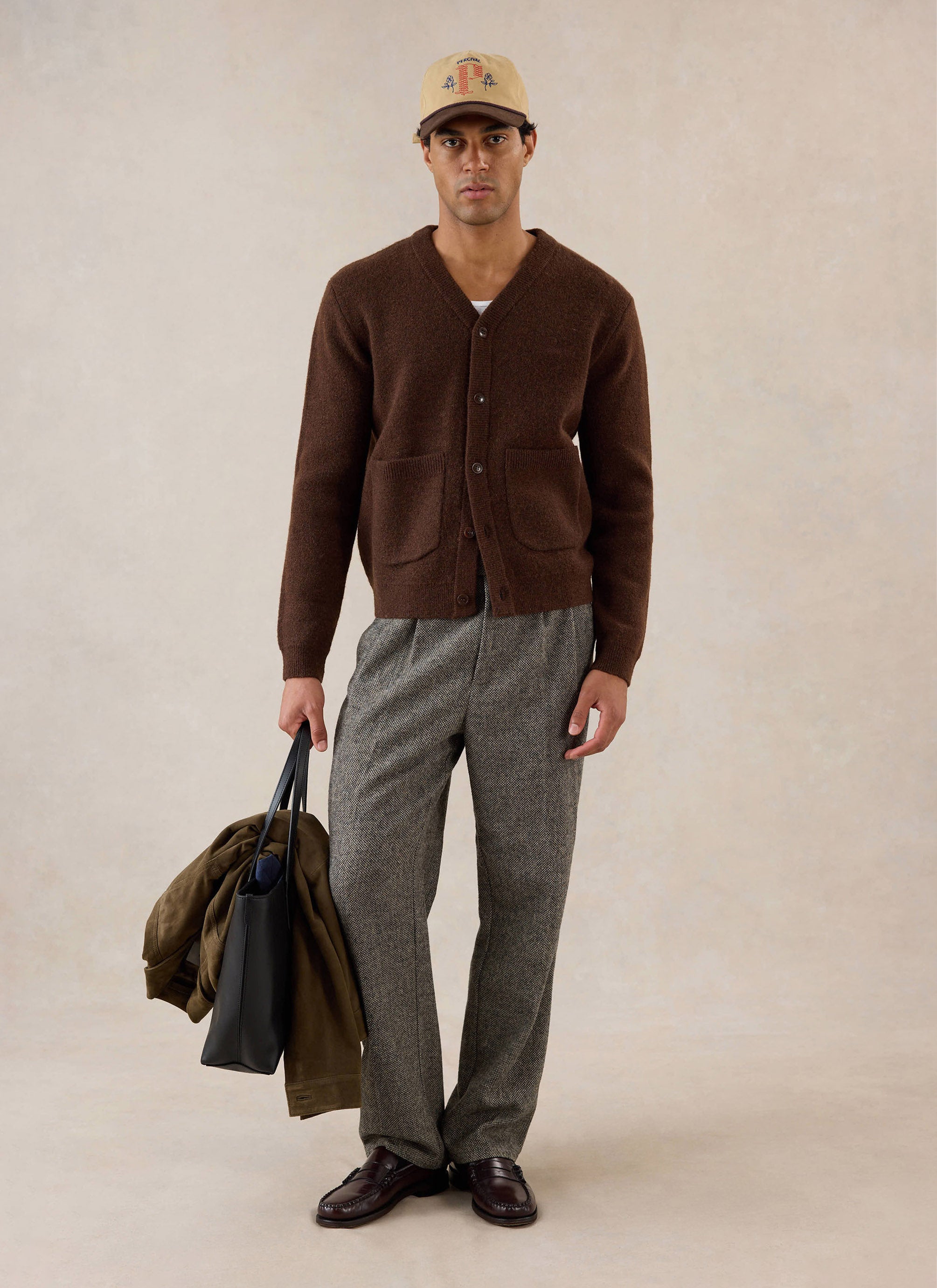 A model wears the Percival espresso mohair White Glove Cardigan, styled with patterned trousers, a cap and a tote bag.