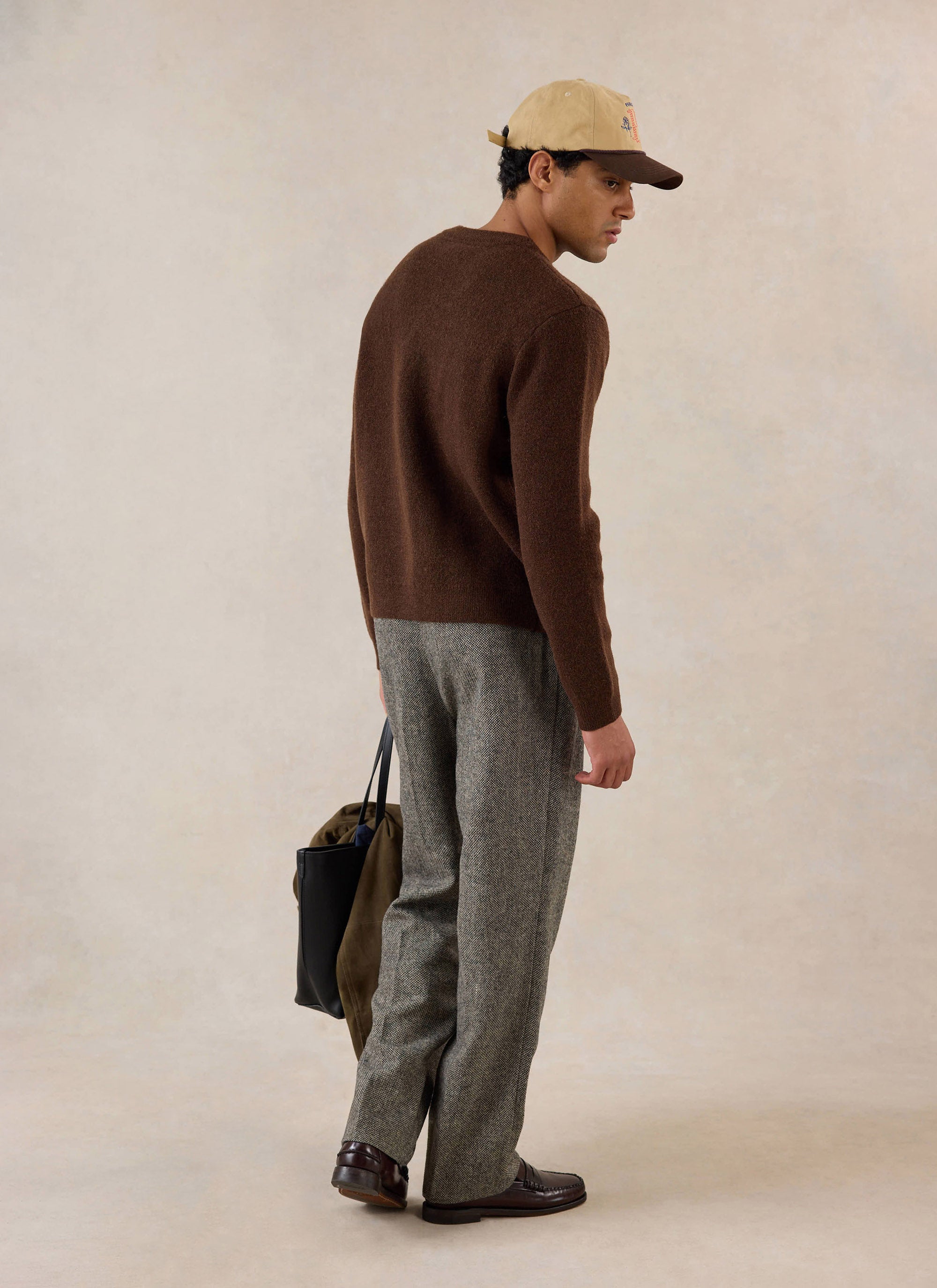 A model from behind wearing the Percival espresso mohair boxy cardigan, tweed trousers, cap, and holding a tote bag.