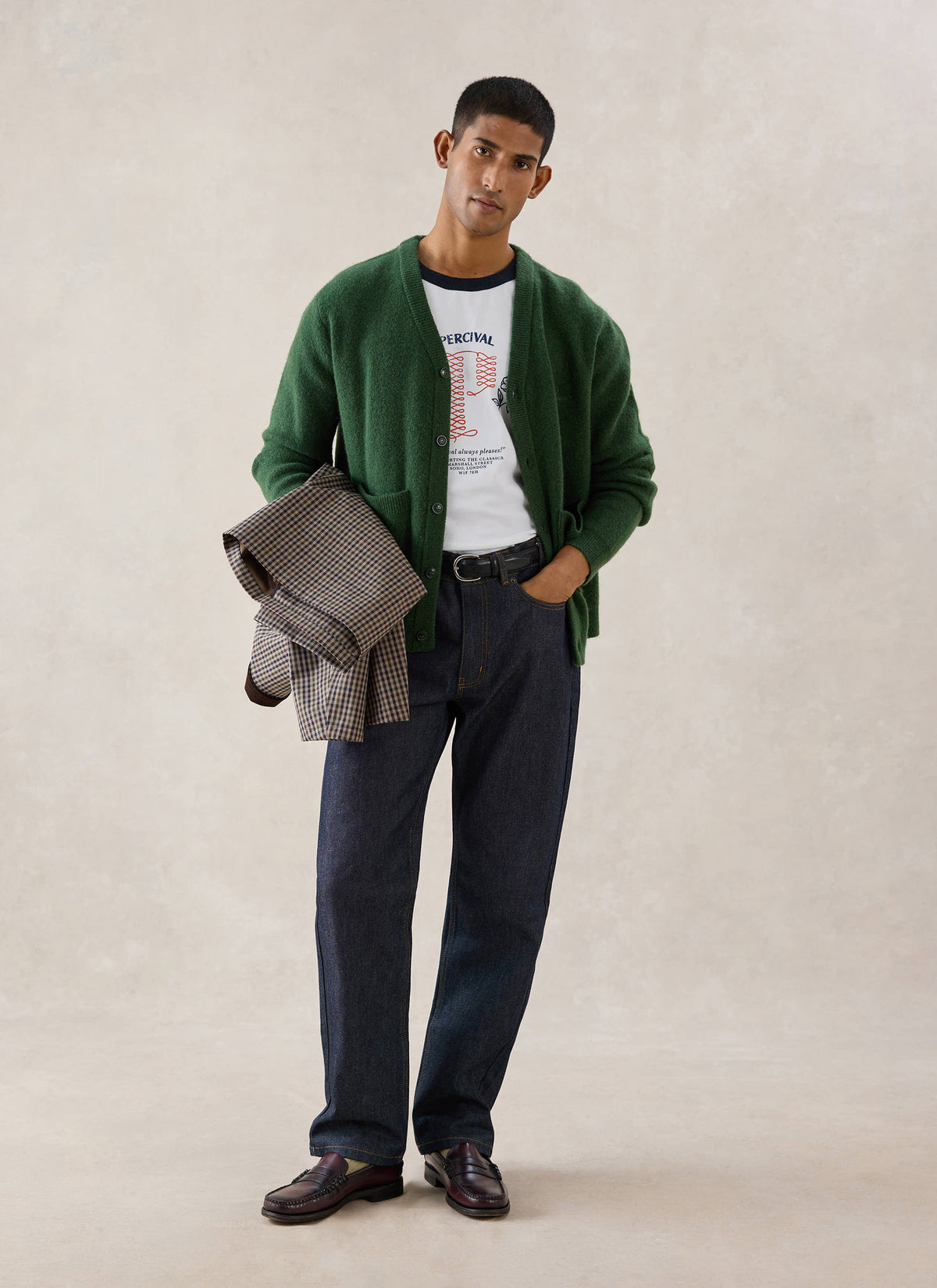 A model wears the Percival forest green mohair cardigan over a white t-shirt and dark jeans while holding a patterned jacket.