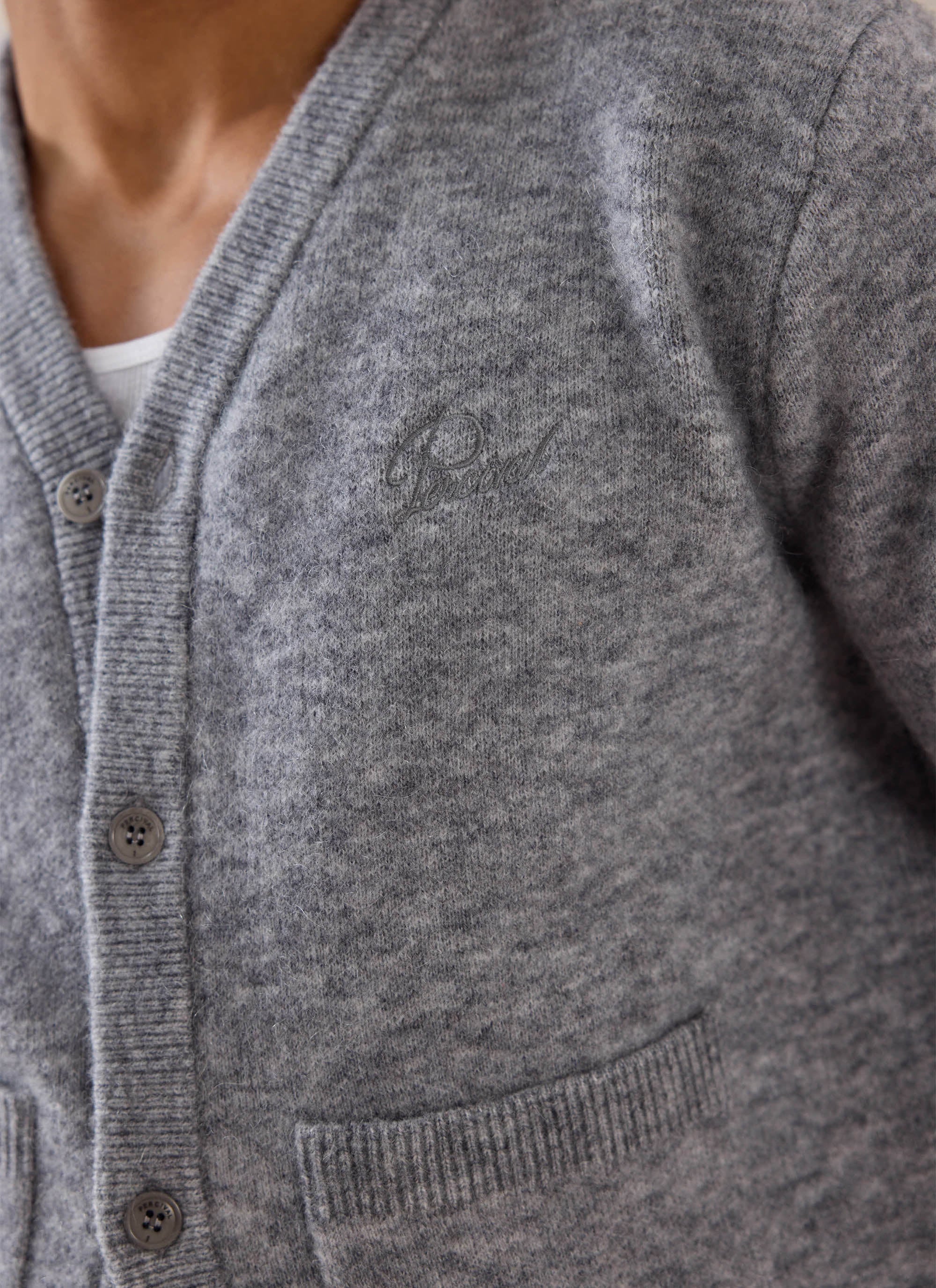 Close-up of a model wearing the grey Percival White Glove mohair cardigan, highlighting the buttons and chest branding.