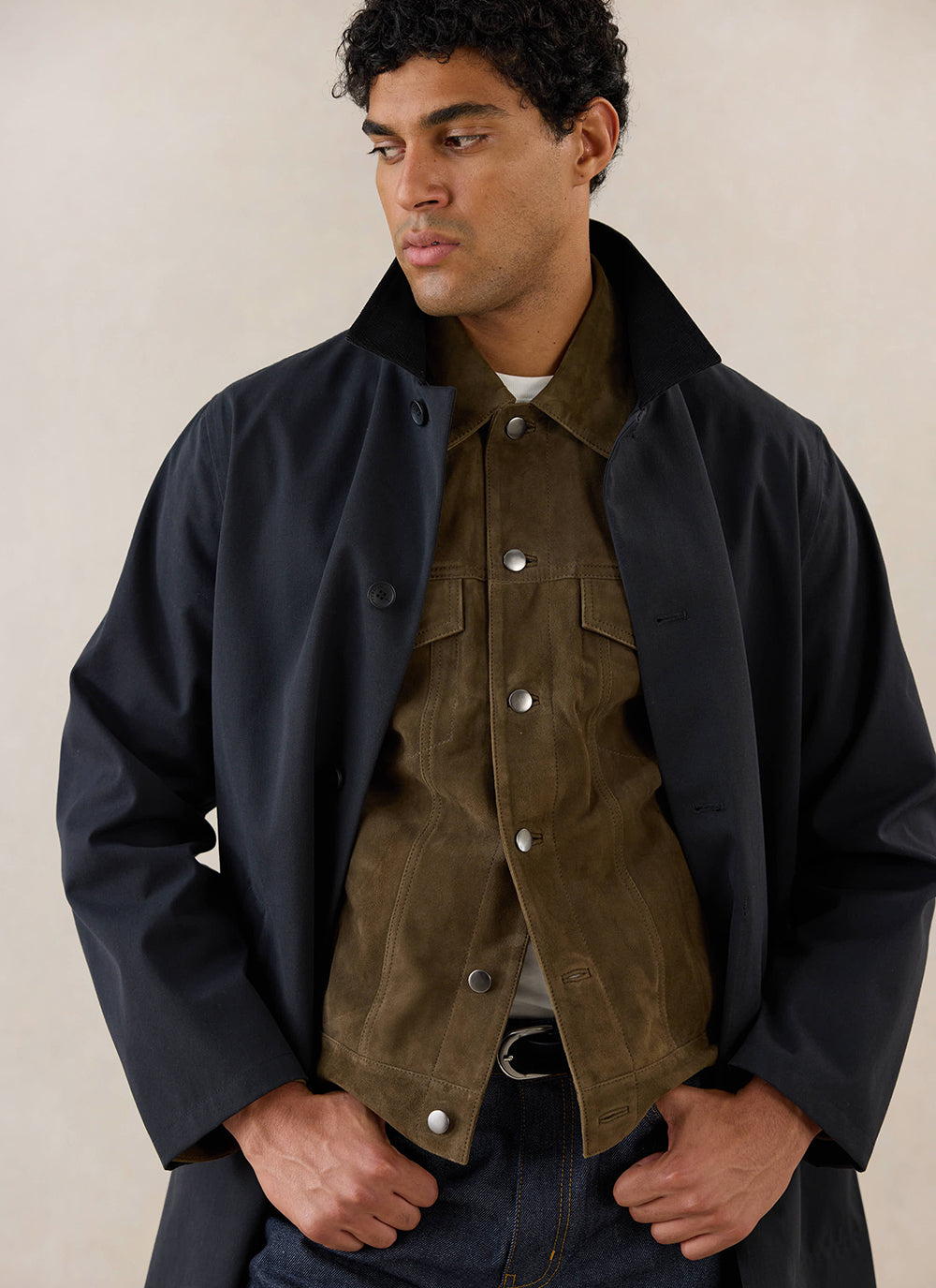 A model wears the black Percival Wilson Long Trench Coat layered over an olive green jacket.