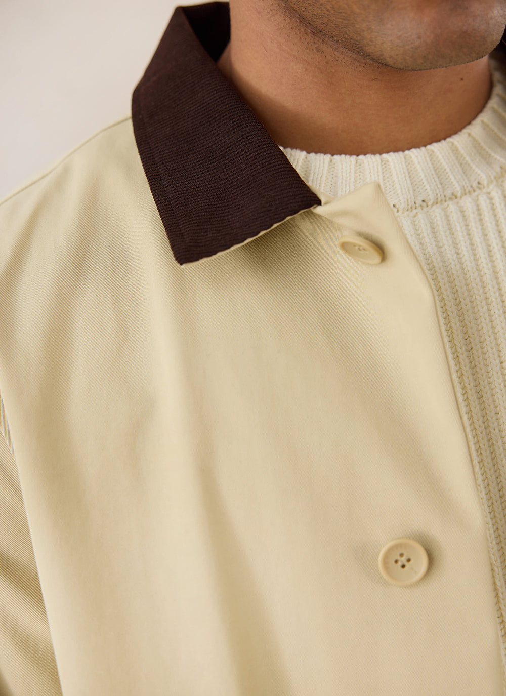 Close-up of the tan Percival Wilson trench coat, highlighting the contrast dark cord collar and button details.