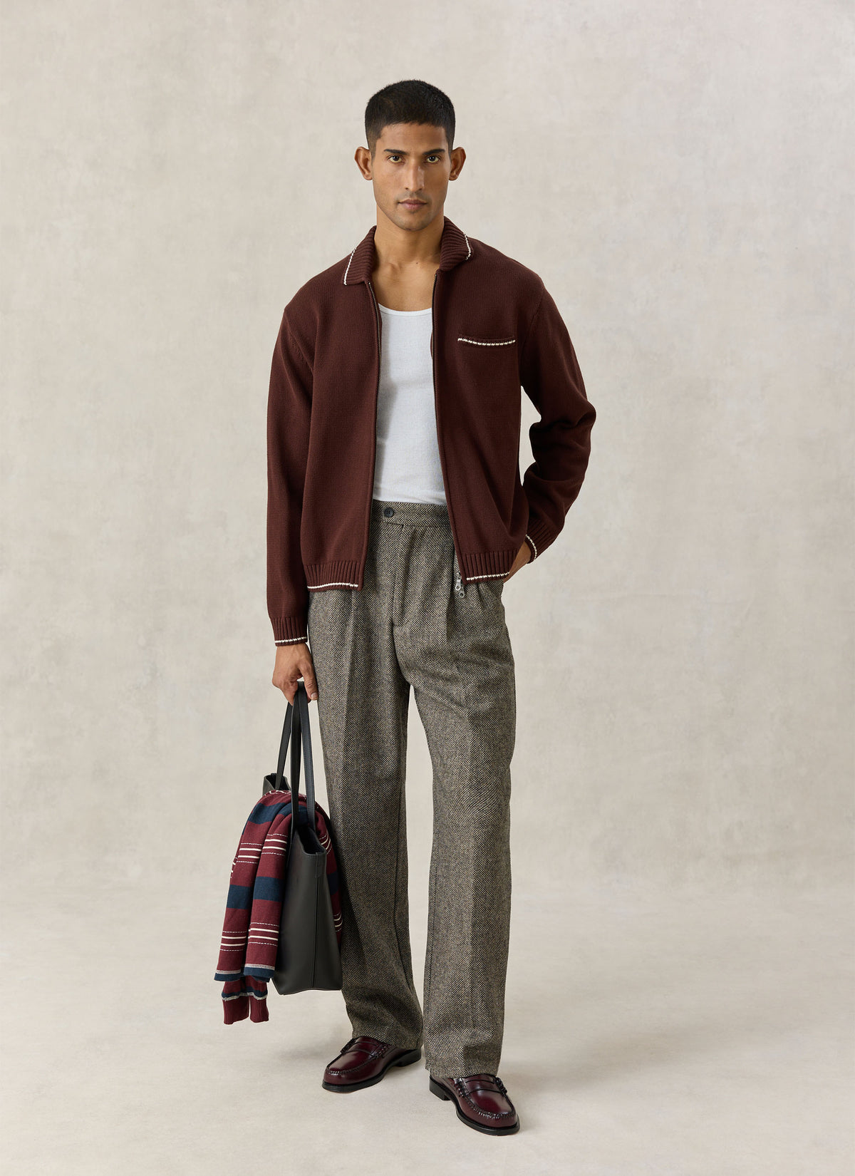 A model wearing the Percival Gardner espresso brown cotton zip cardigan with tailored trousers and a tote bag.