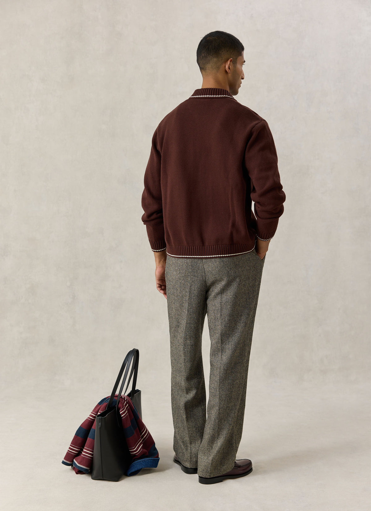 A model from the back wearing the Percival espresso brown cotton zip cardigan with tipping, trousers, and a tote bag.