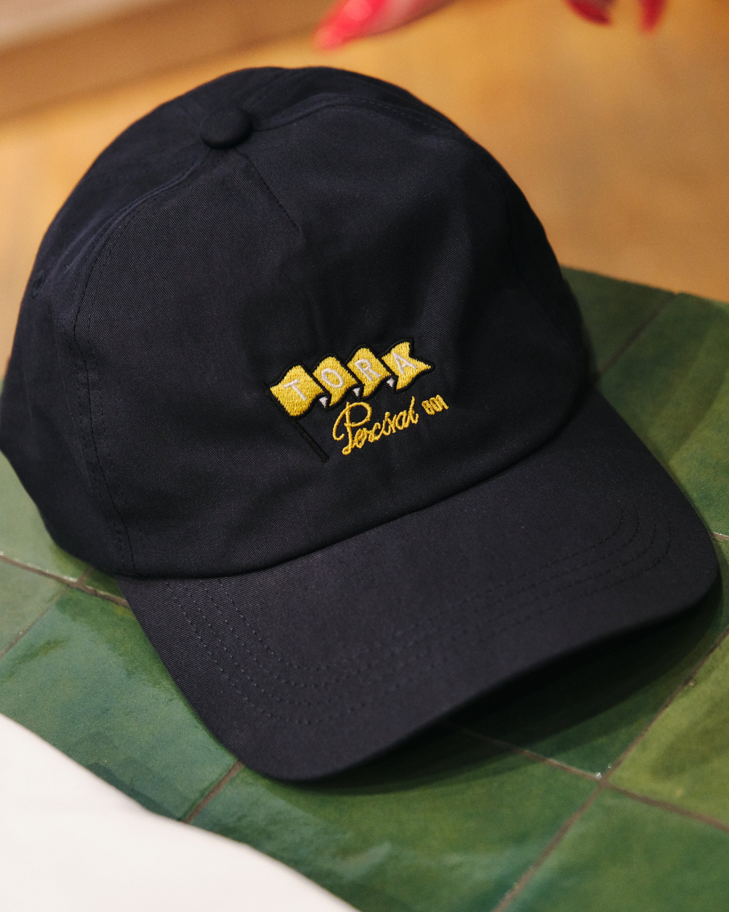 Limited edition men's black cap with custom yellow embroidery, exclusive to the Percival pop-up store inside Selfridges Birmingham.