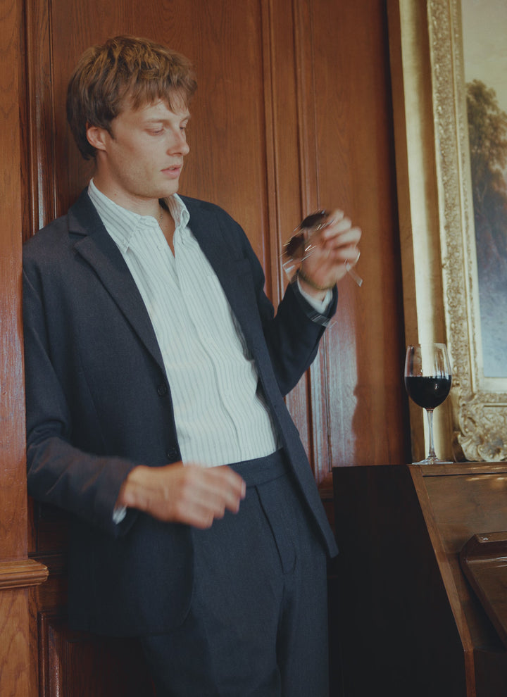A model wears the Percival Stanley pleated tailored trousers in navy herringbone wool, styled as a full suit.
