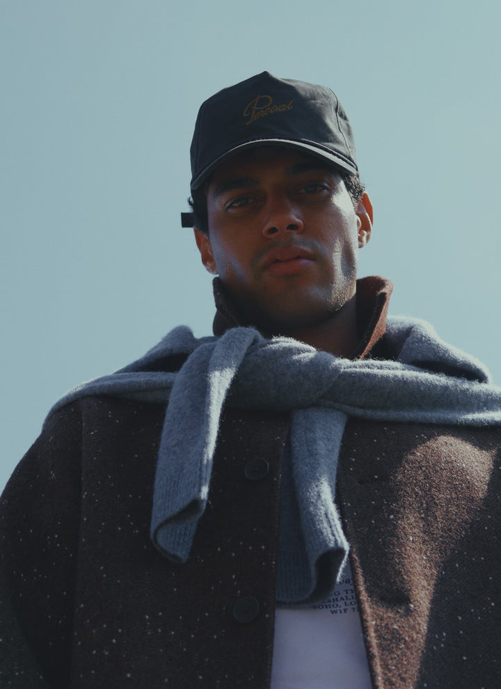 A model wearing the charcoal Percival soft trucker cap, styled with an overcoat and a jumper over shoulders.