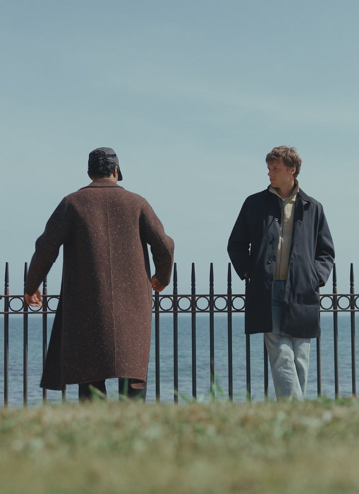 Two models in Percival outerwear by the sea, showcasing the Minnesota overcoat and Wilson trench coat.