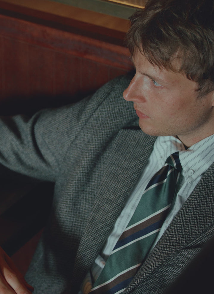A model wears the Percival forest multi stripe silk tie, styled with a grey textured blazer and a striped shirt.