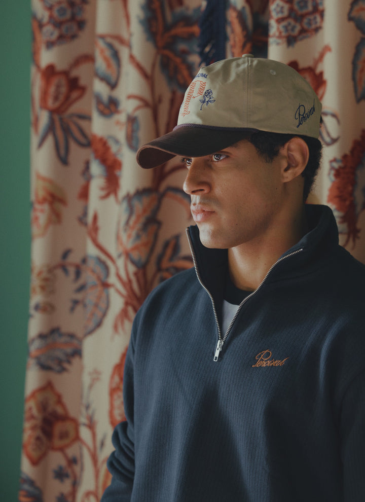 A model wears the navy cotton Percival Conrad funnel neck 1/4 zip jumper with a cap.