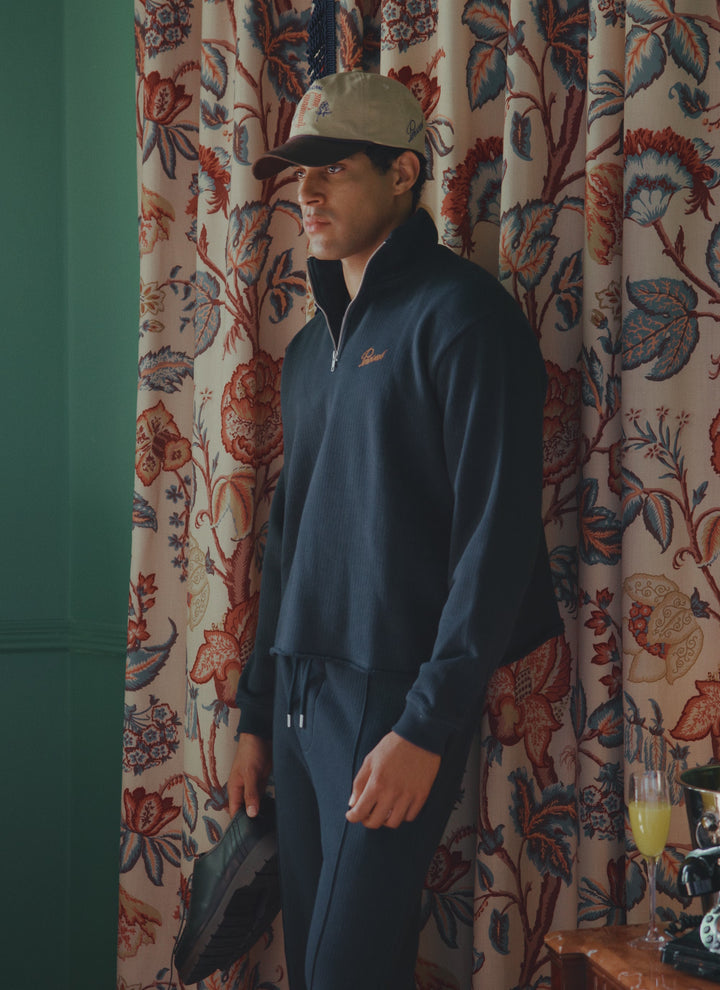A model wearing the Percival navy cotton Conrad Funnel Neck 1/4 Zip Jumper and matching trackpants with a cap.
