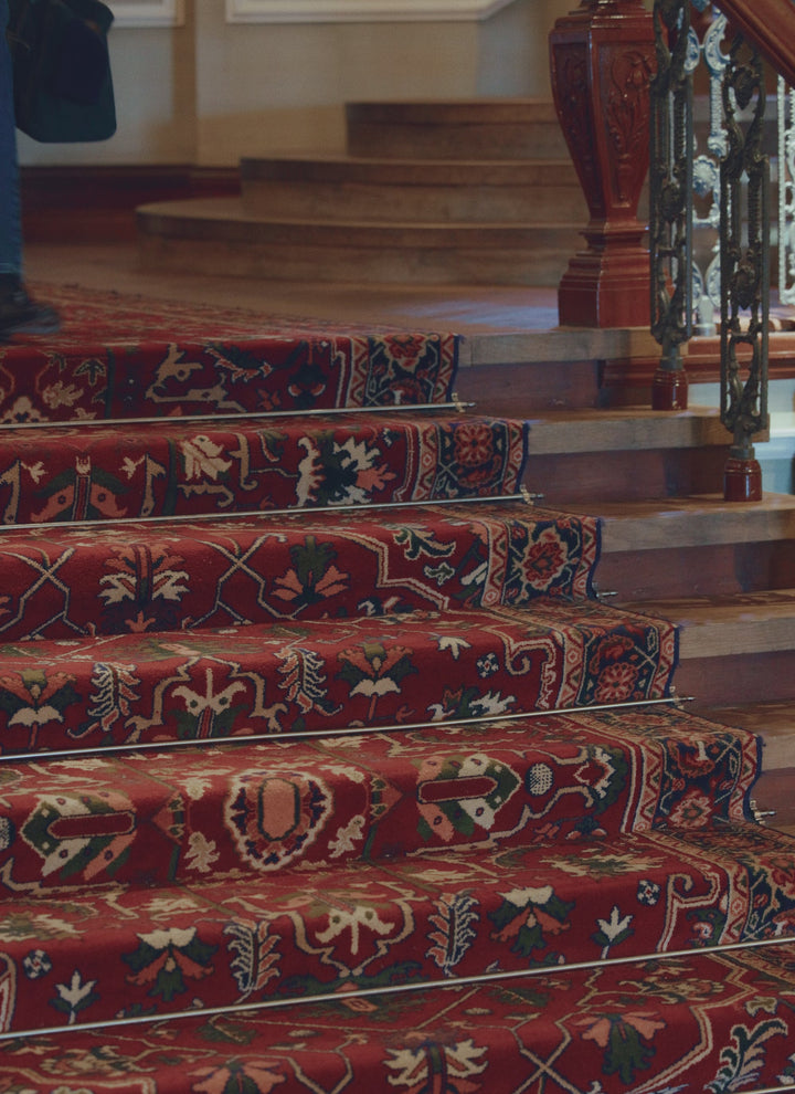 A model walks down a carpeted staircase wearing the blue Rhodes crew neck jumper from Percival.