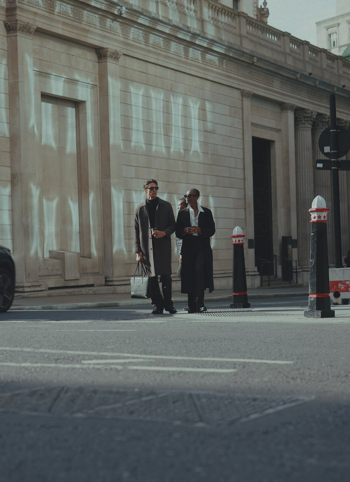 Two models walking across a city street, one wearing the Percival black wool blend double-breasted overcoat.